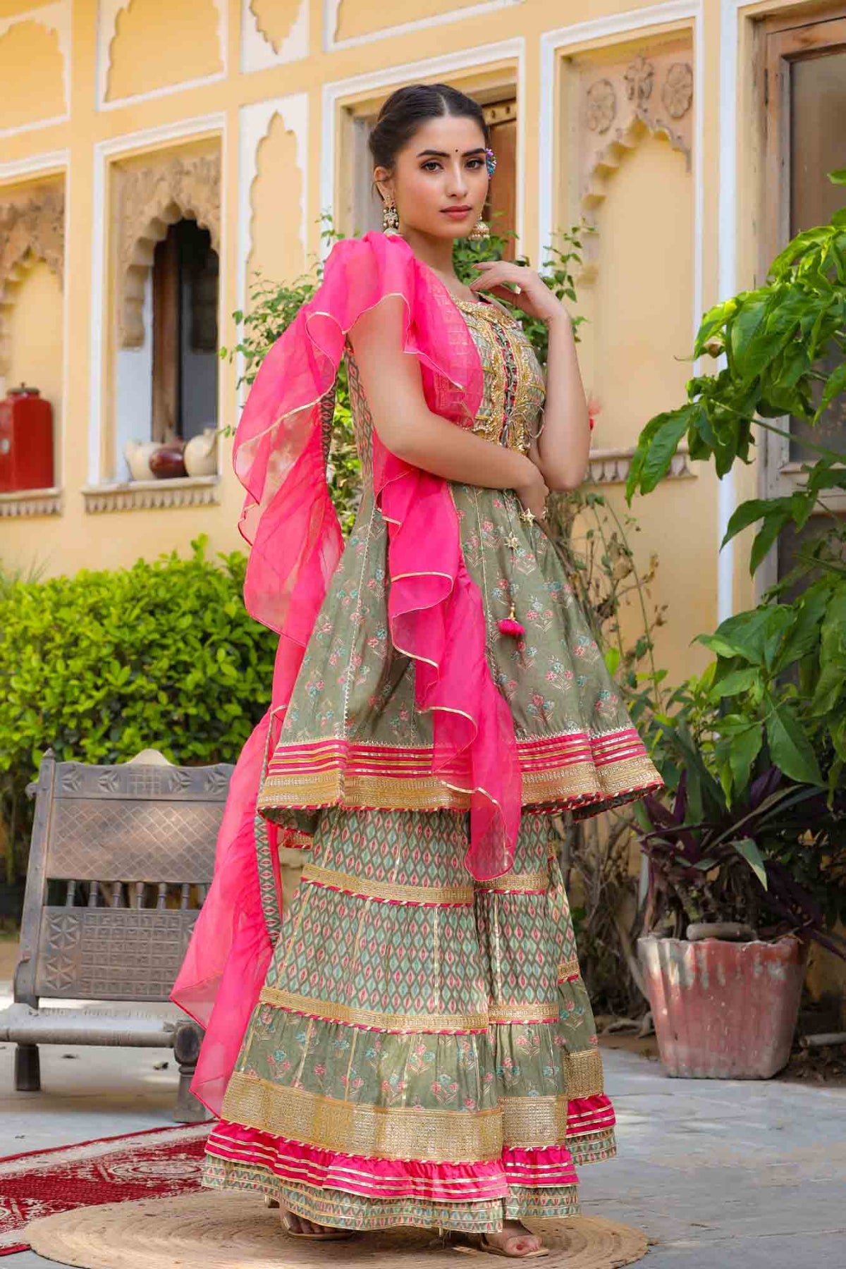Woman in traditional outfit with pink dupatta standing outdoors.