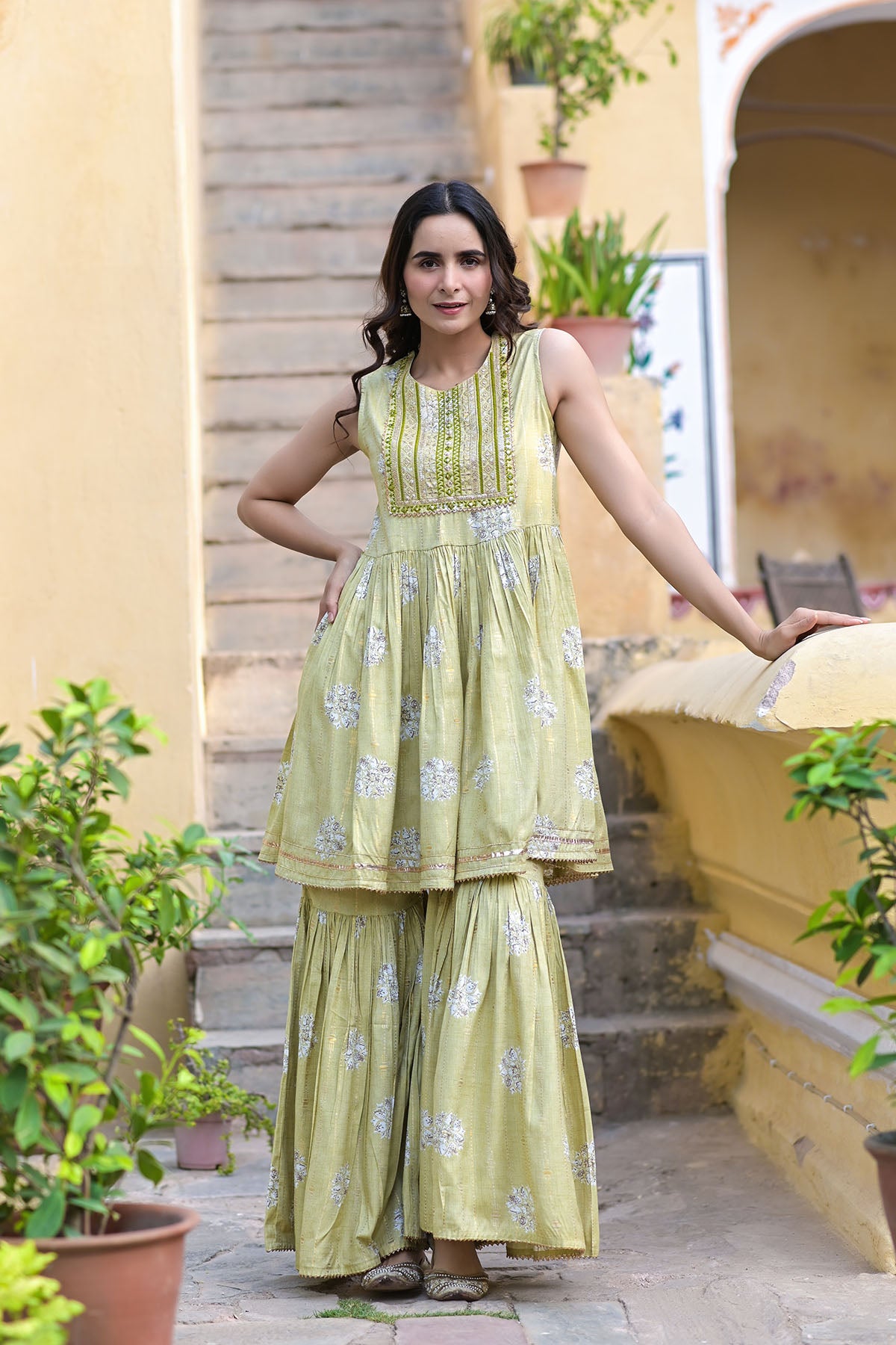 Woman in a light green dress standing outdoors with plants and a yellow wall in the background