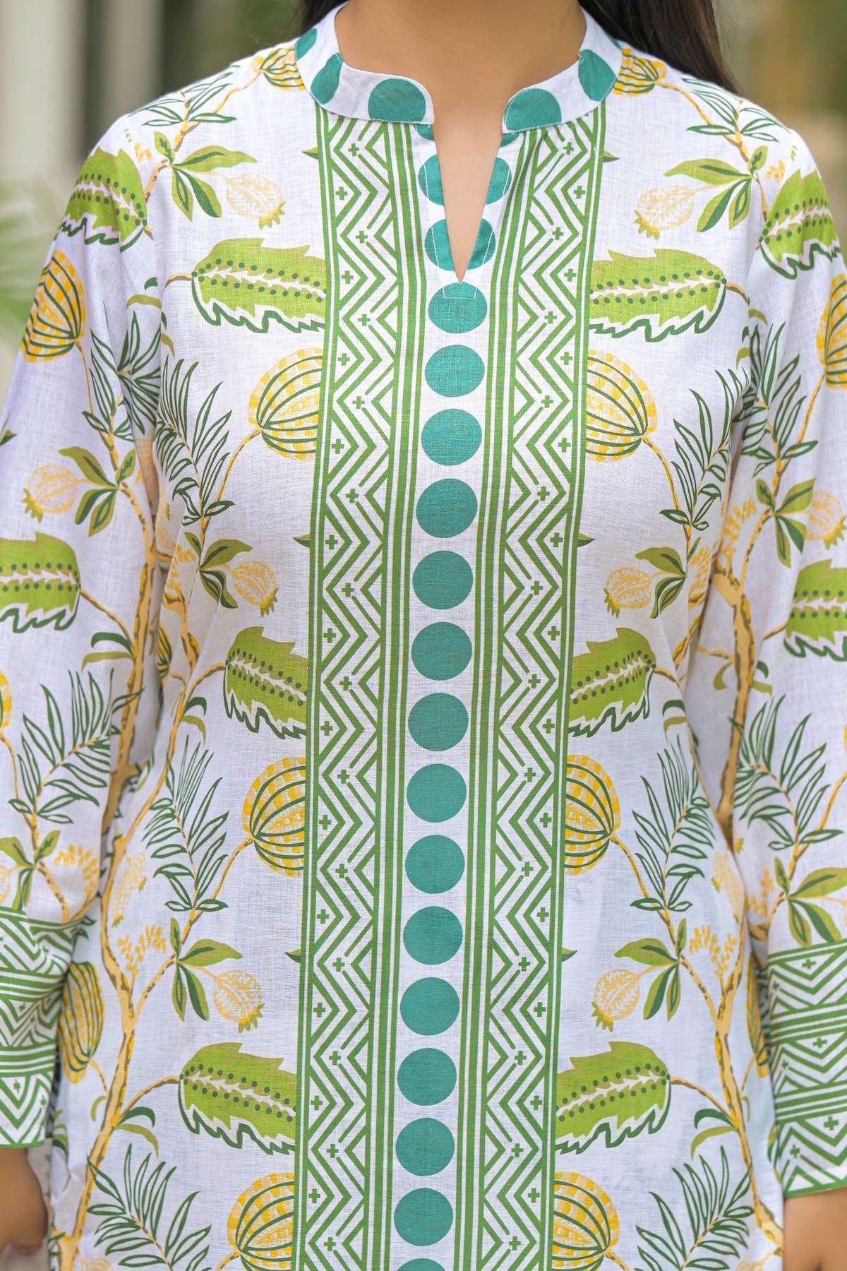 White garment with green and yellow floral and geometric patterns on a mannequin.