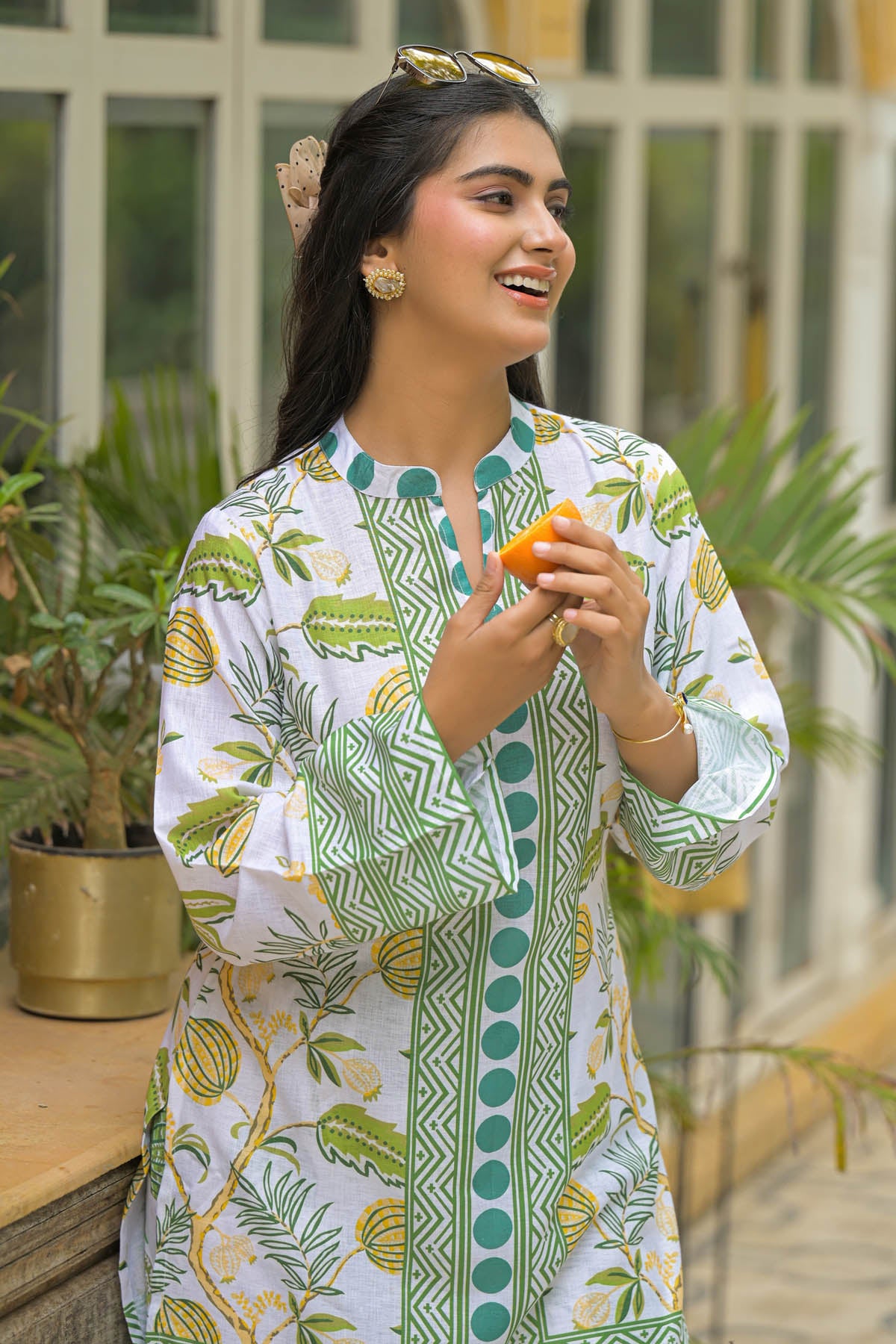 Woman wearing a patterned dress holding an orange outdoors