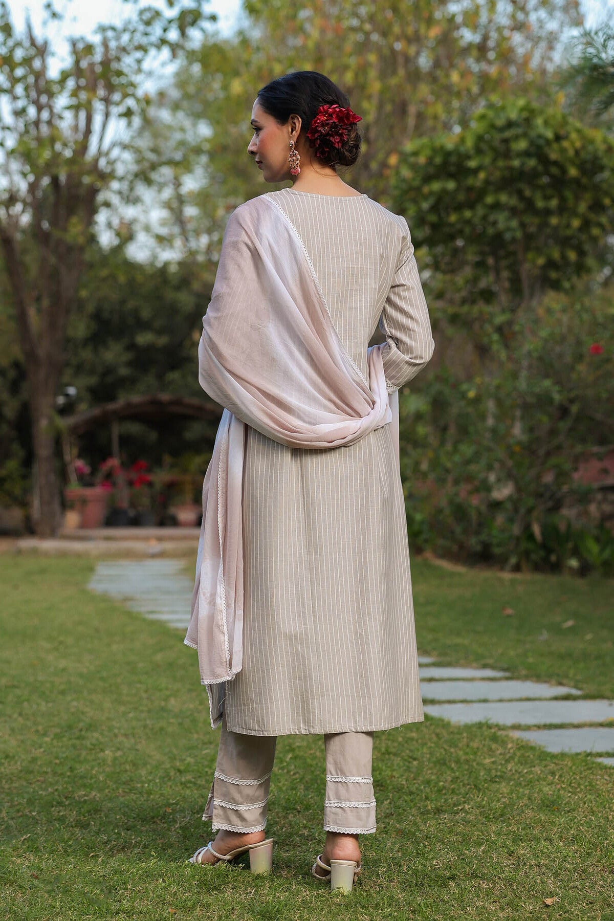 Woman in a light-colored traditional outfit standing in a garden.