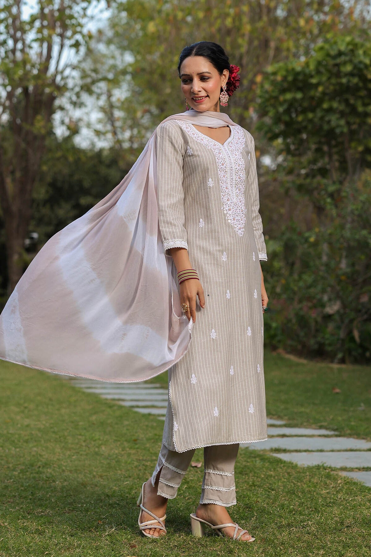 Woman in a light-colored traditional outfit standing outdoors with greenery in the background