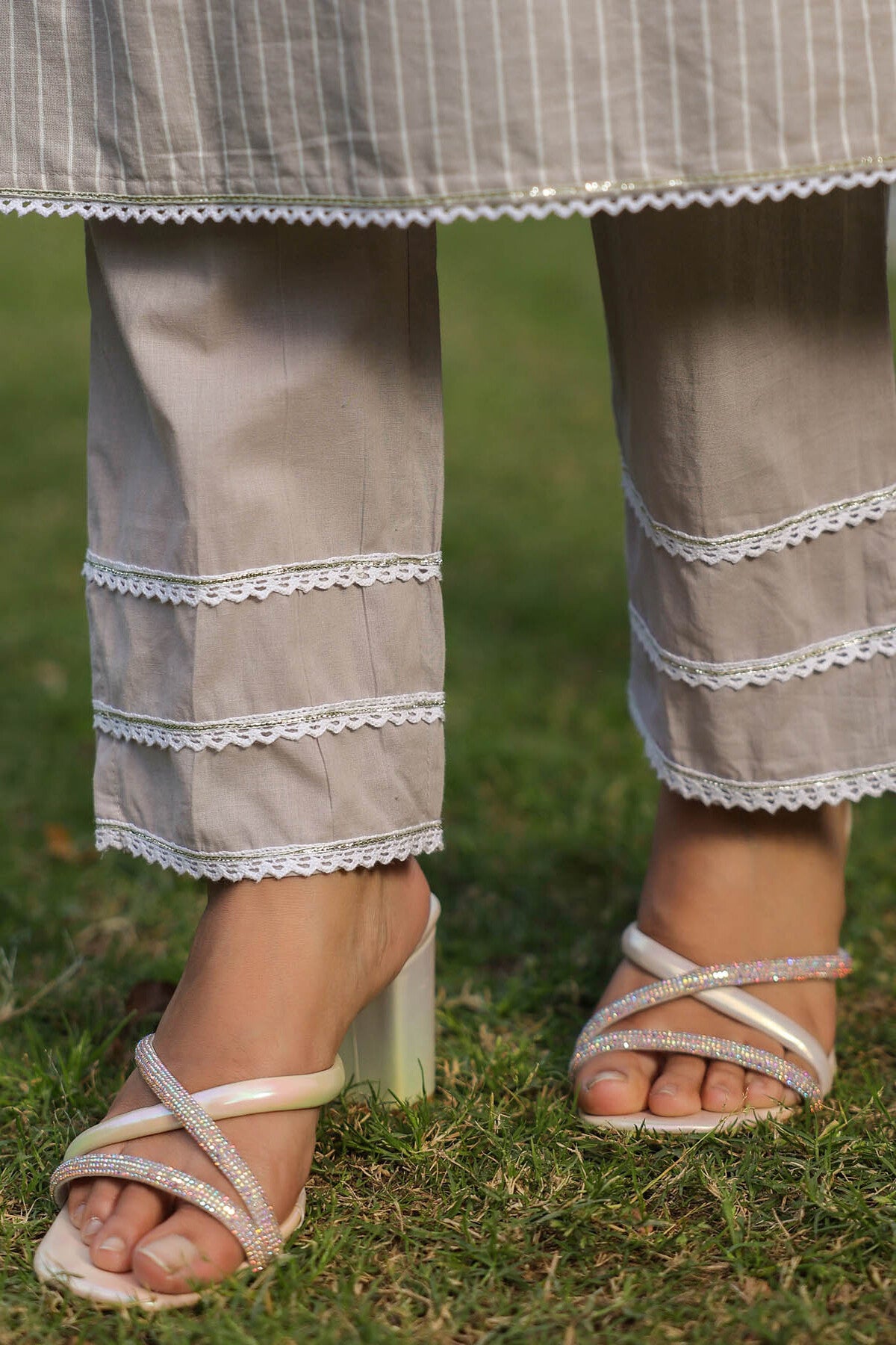 Person wearing light-colored pants with lace trim and sandals on grass