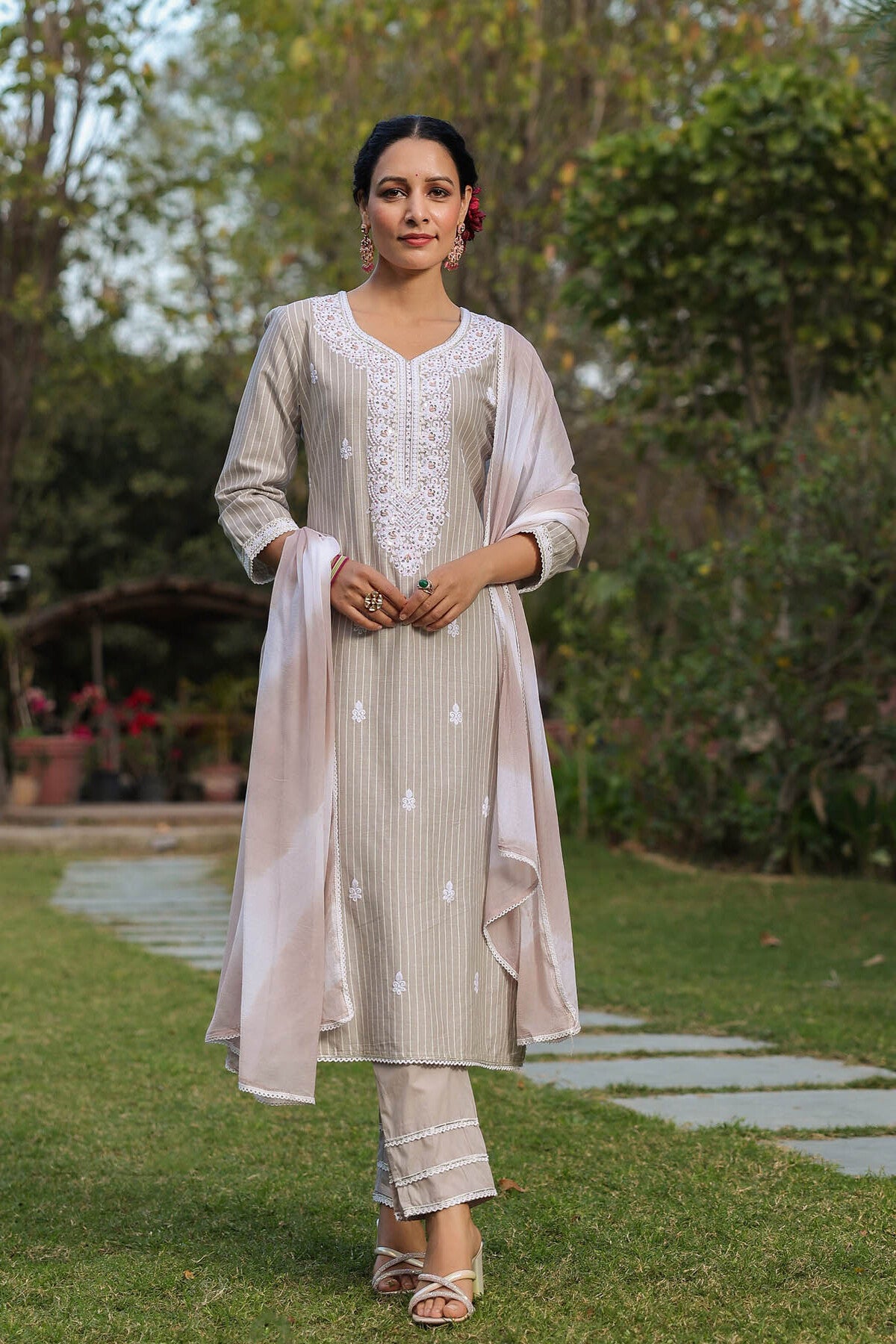Woman in a light-colored traditional outfit standing in a garden.