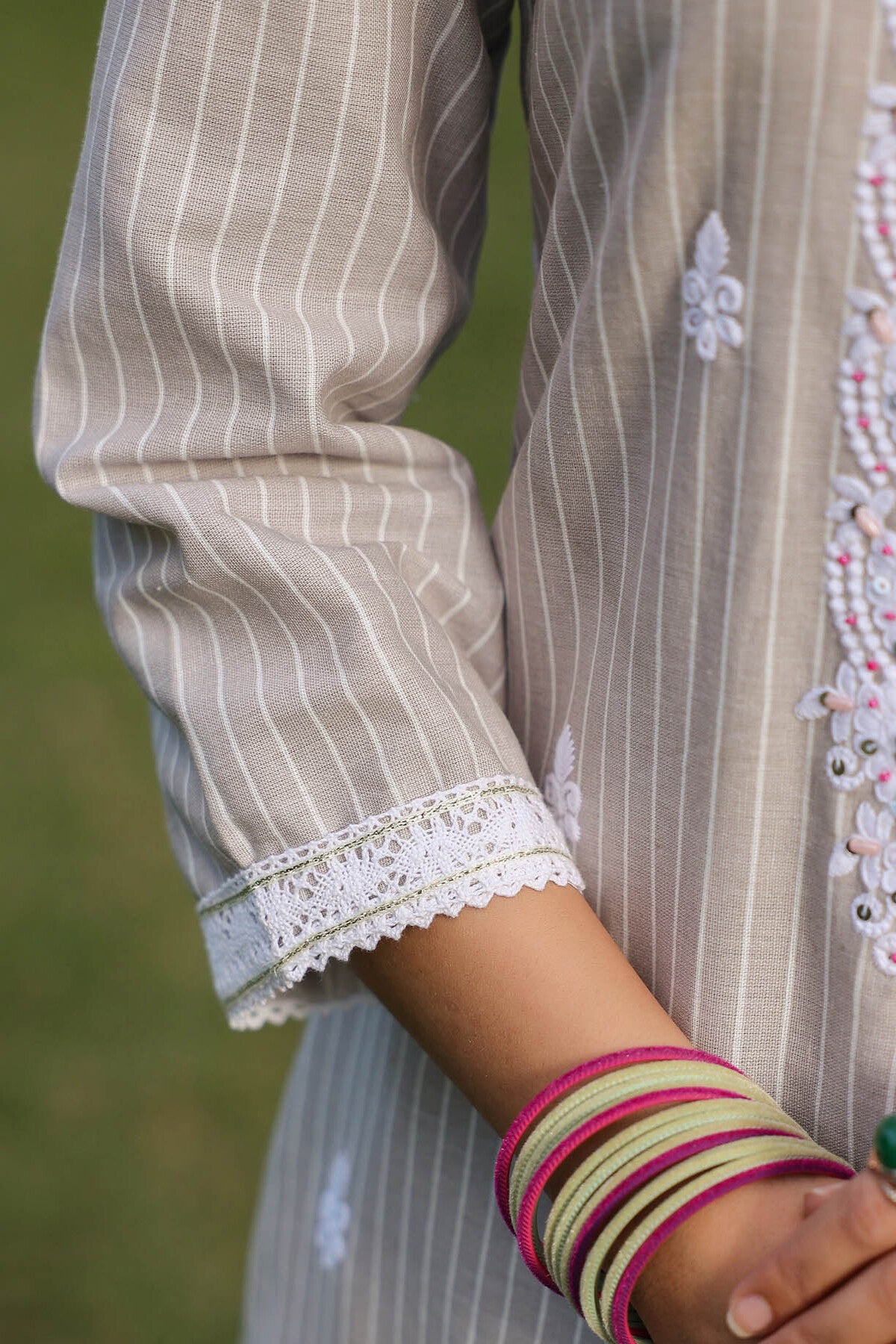 Close-up of a person wearing a traditional outfit with lace cuffs and colorful bangles.