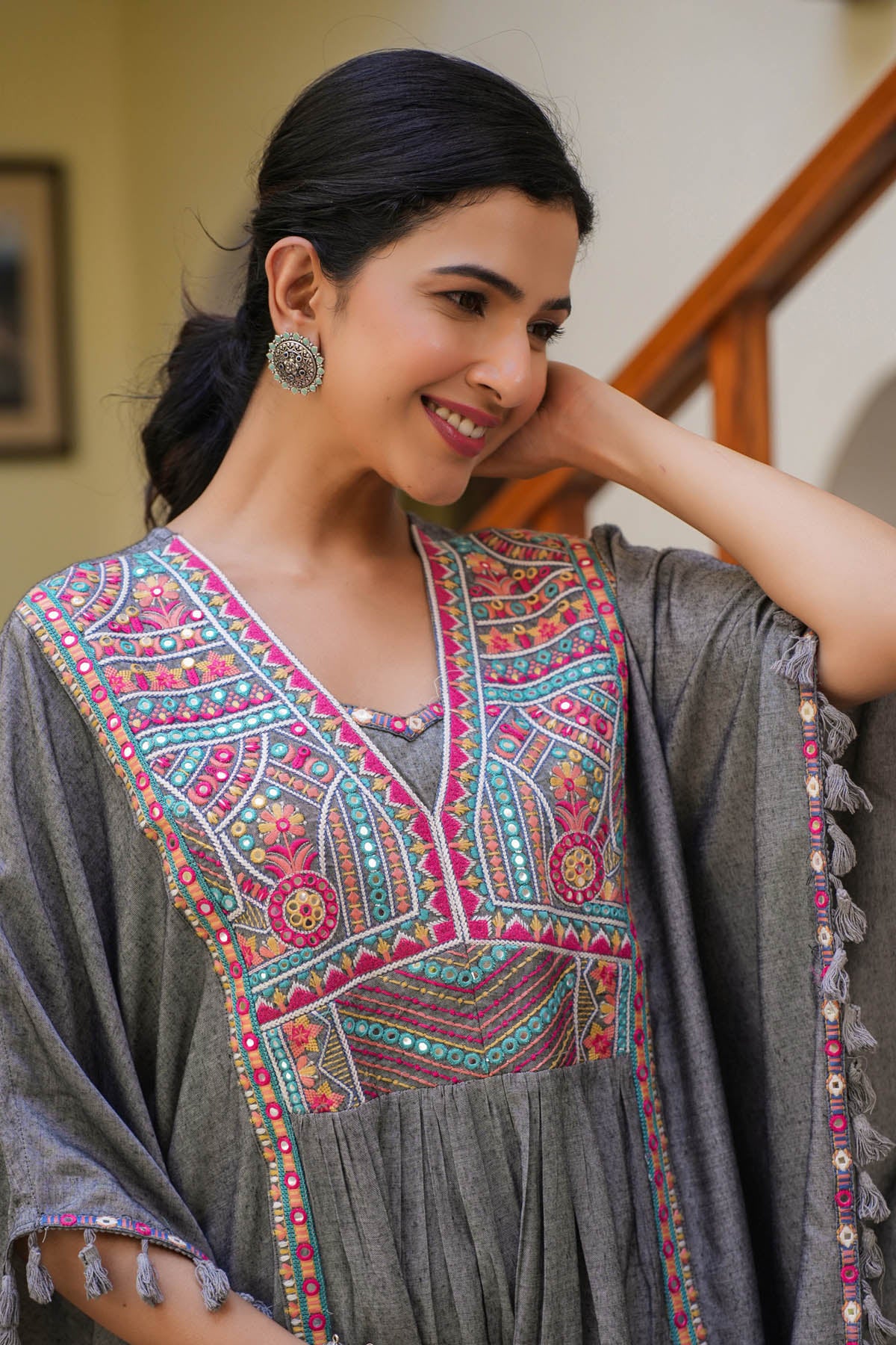 Woman wearing a traditional embroidered dress with a gray shawl indoors.