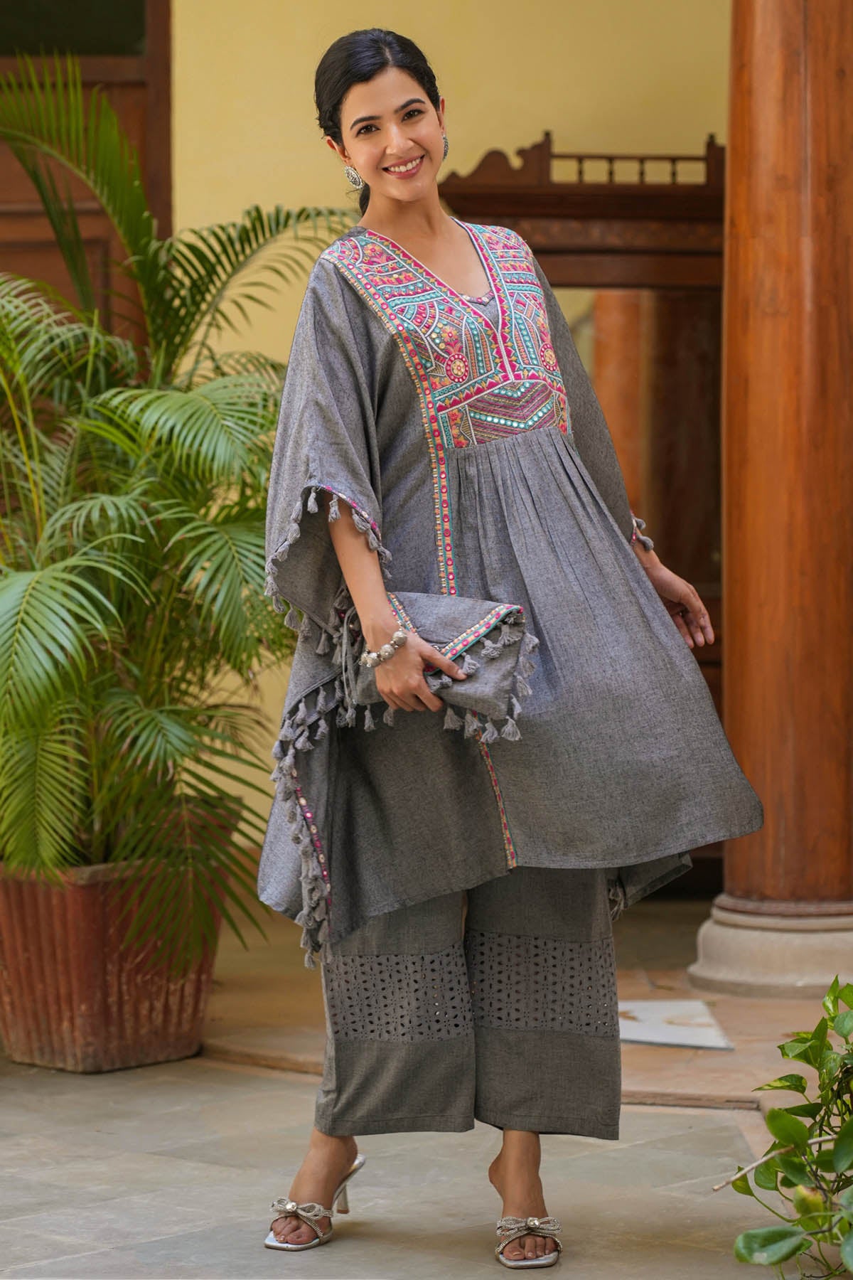 Woman in a traditional outfit standing in a decorated indoor setting with plants.