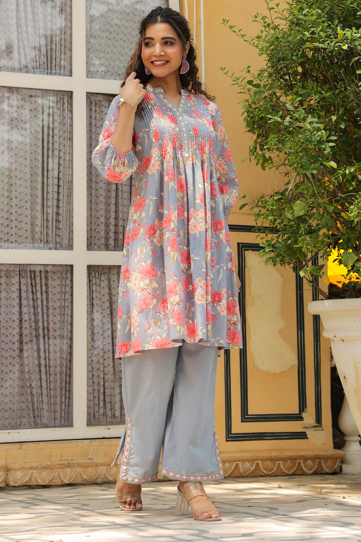 Woman wearing a floral dress and light blue pants standing outdoors.