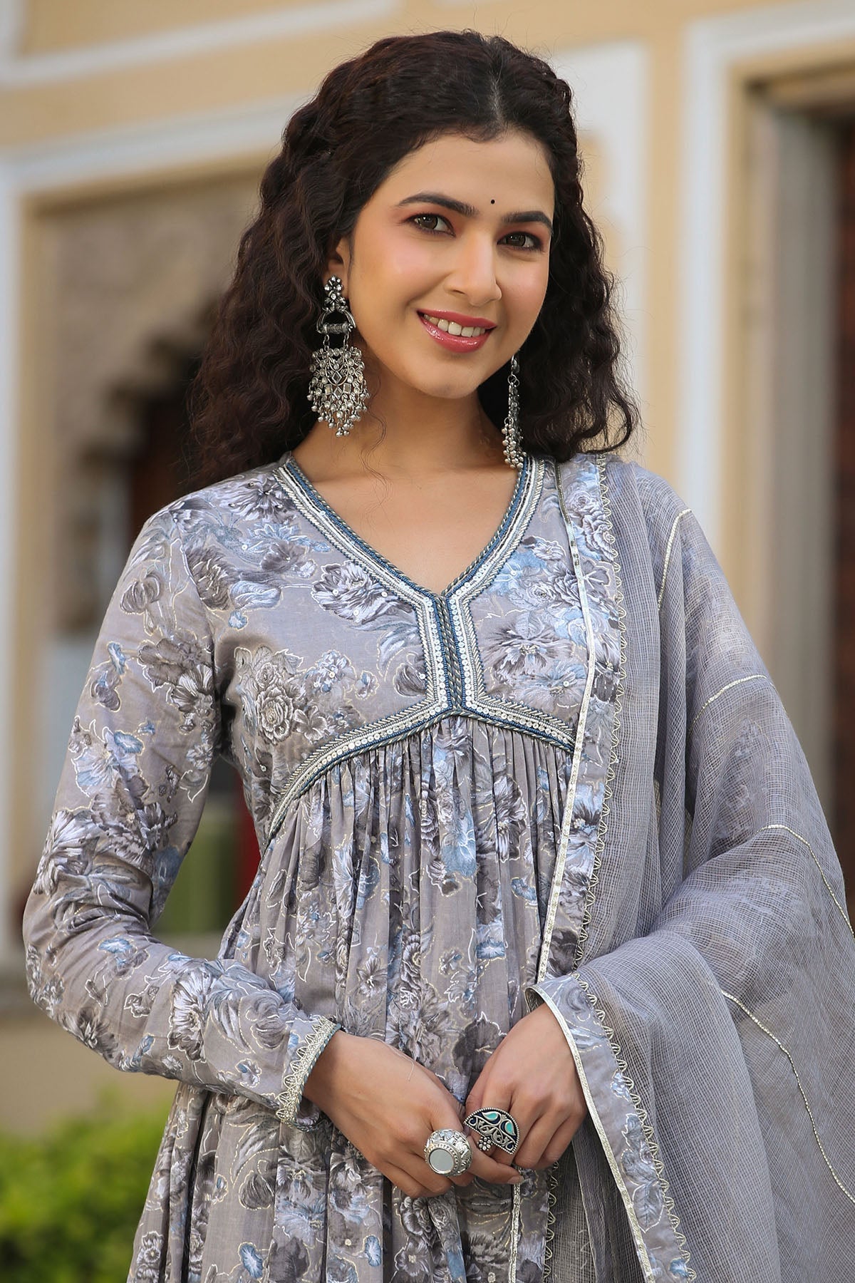 Woman in traditional attire with jewelry, standing outdoors.