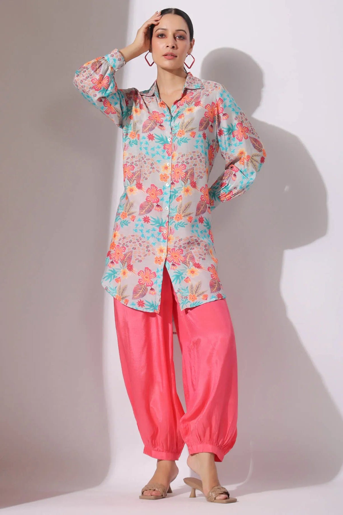 Woman wearing a colorful floral top and pink pants against a white background