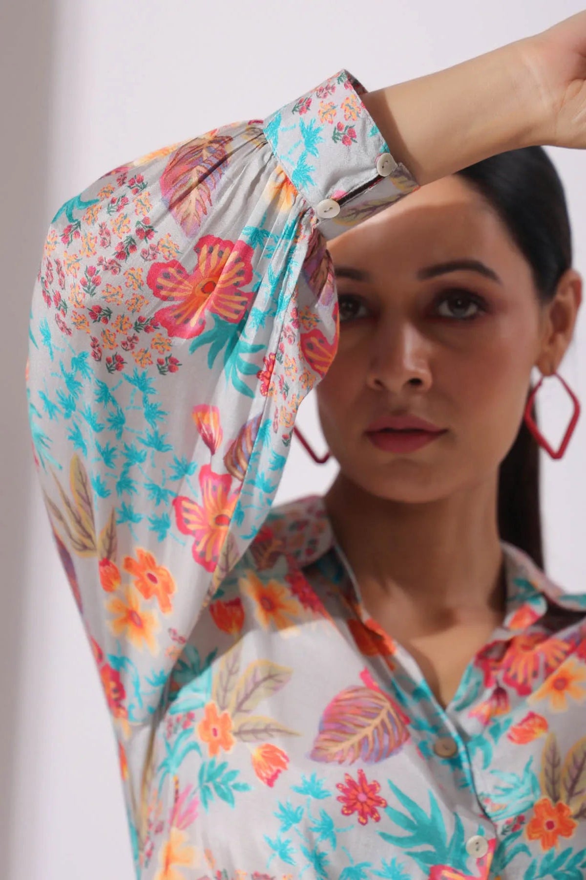 Woman wearing a colorful floral headscarf and shirt against a plain background