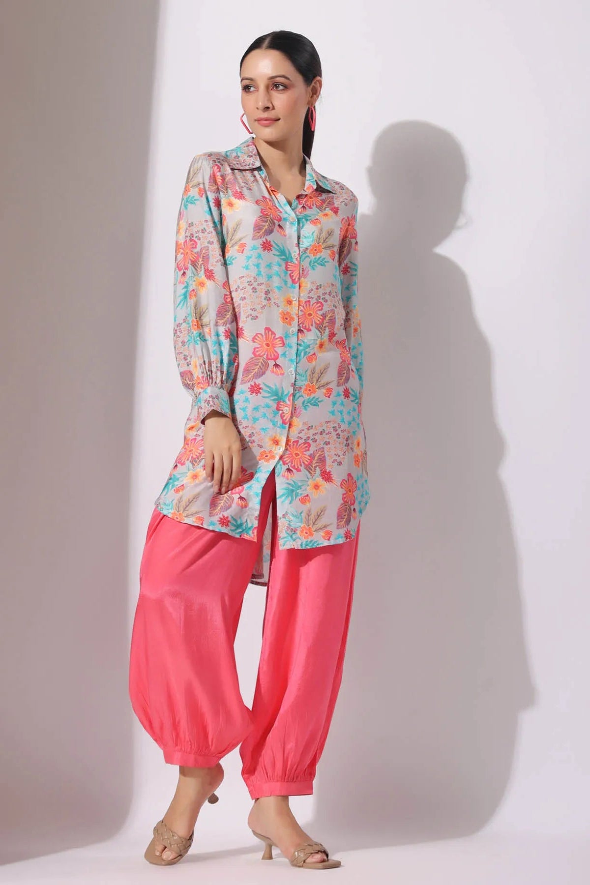 Woman wearing a colorful floral shirt and pink pants against a white background