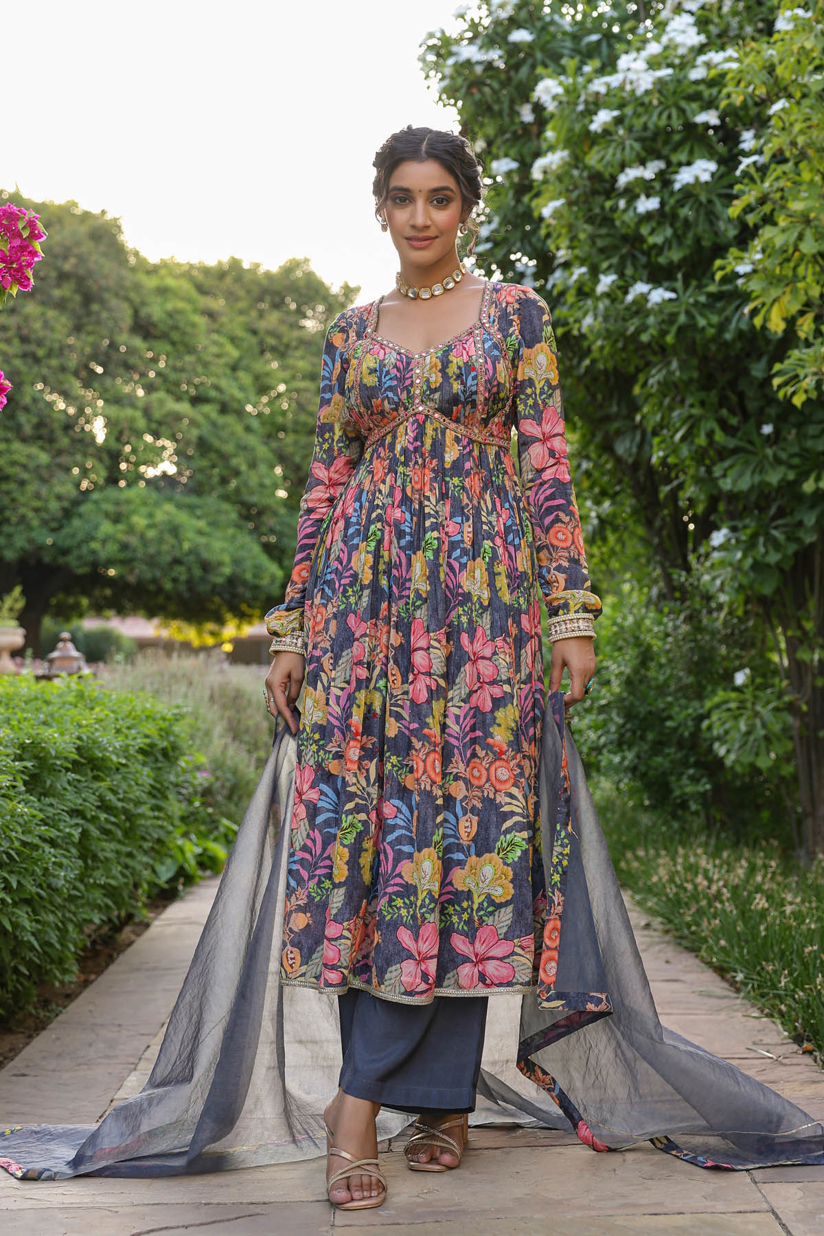 Woman in a colorful floral dress standing outdoors with greenery in the background