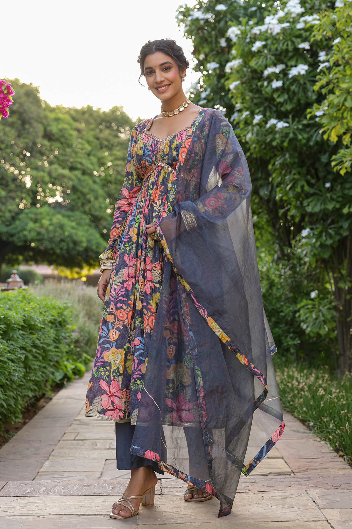 Woman in a colorful floral dress with a matching shawl standing outdoors.