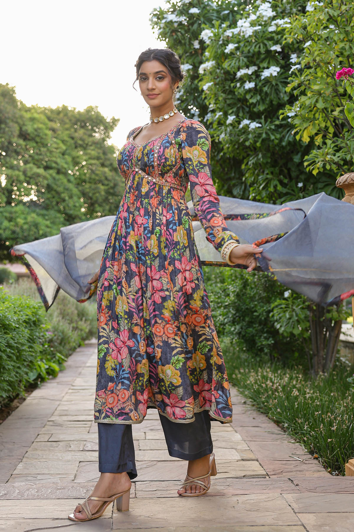 Woman in a colorful floral dress standing outdoors with greenery in the background