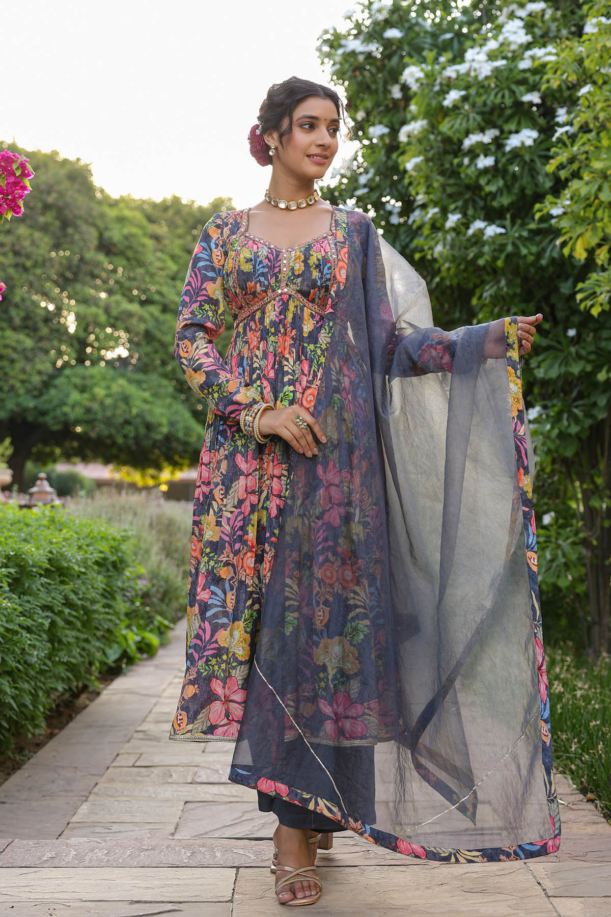Woman in a colorful floral dress with a matching dupatta standing outdoors.