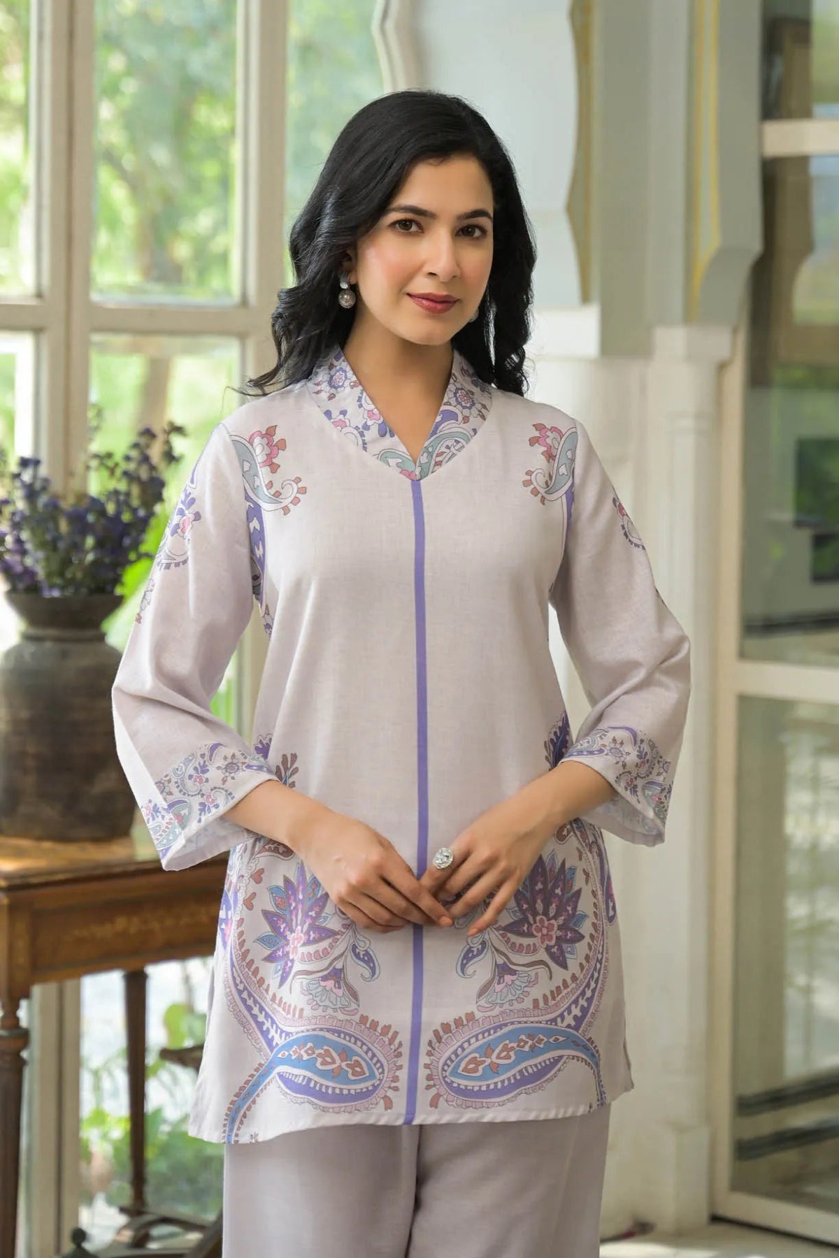 Woman wearing a light gray embroidered blouse with a floral pattern in a bright indoor setting.