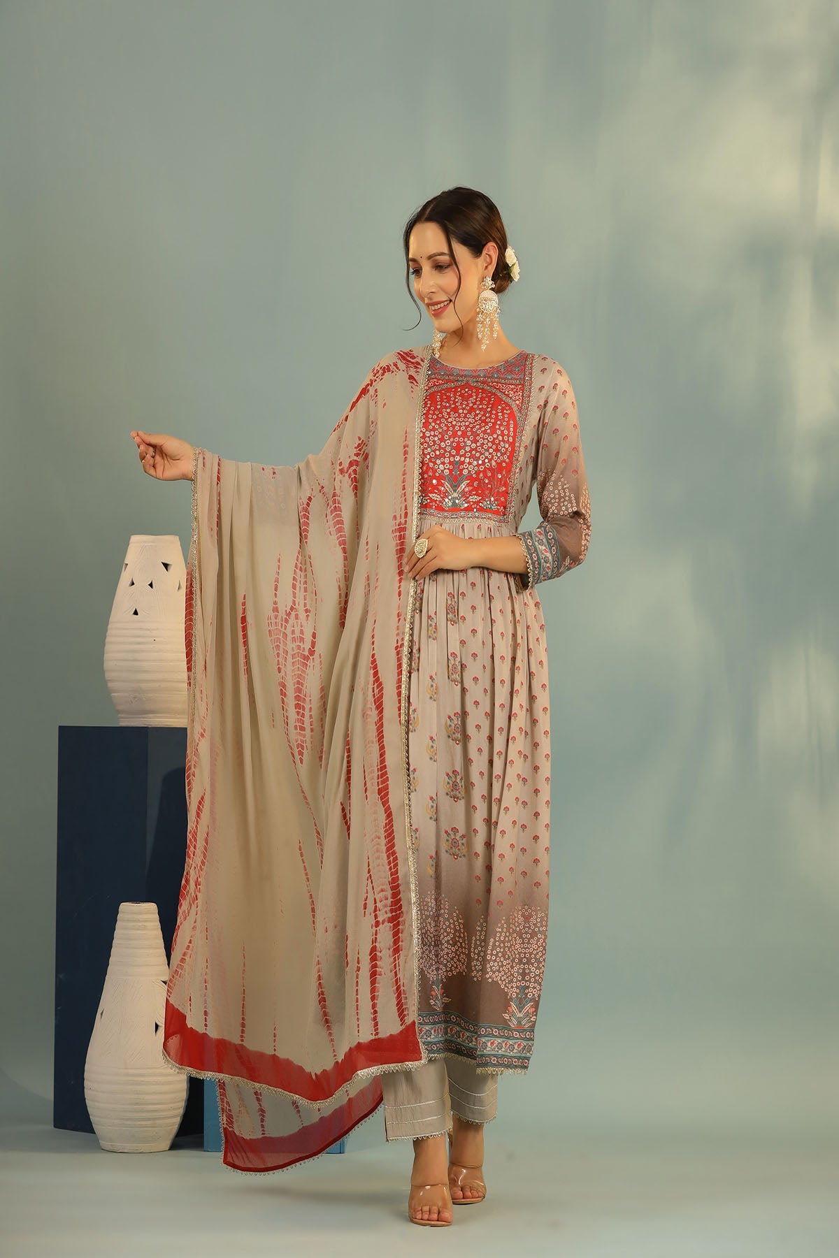 Woman in traditional outfit with red and beige patterns, standing against a neutral background.