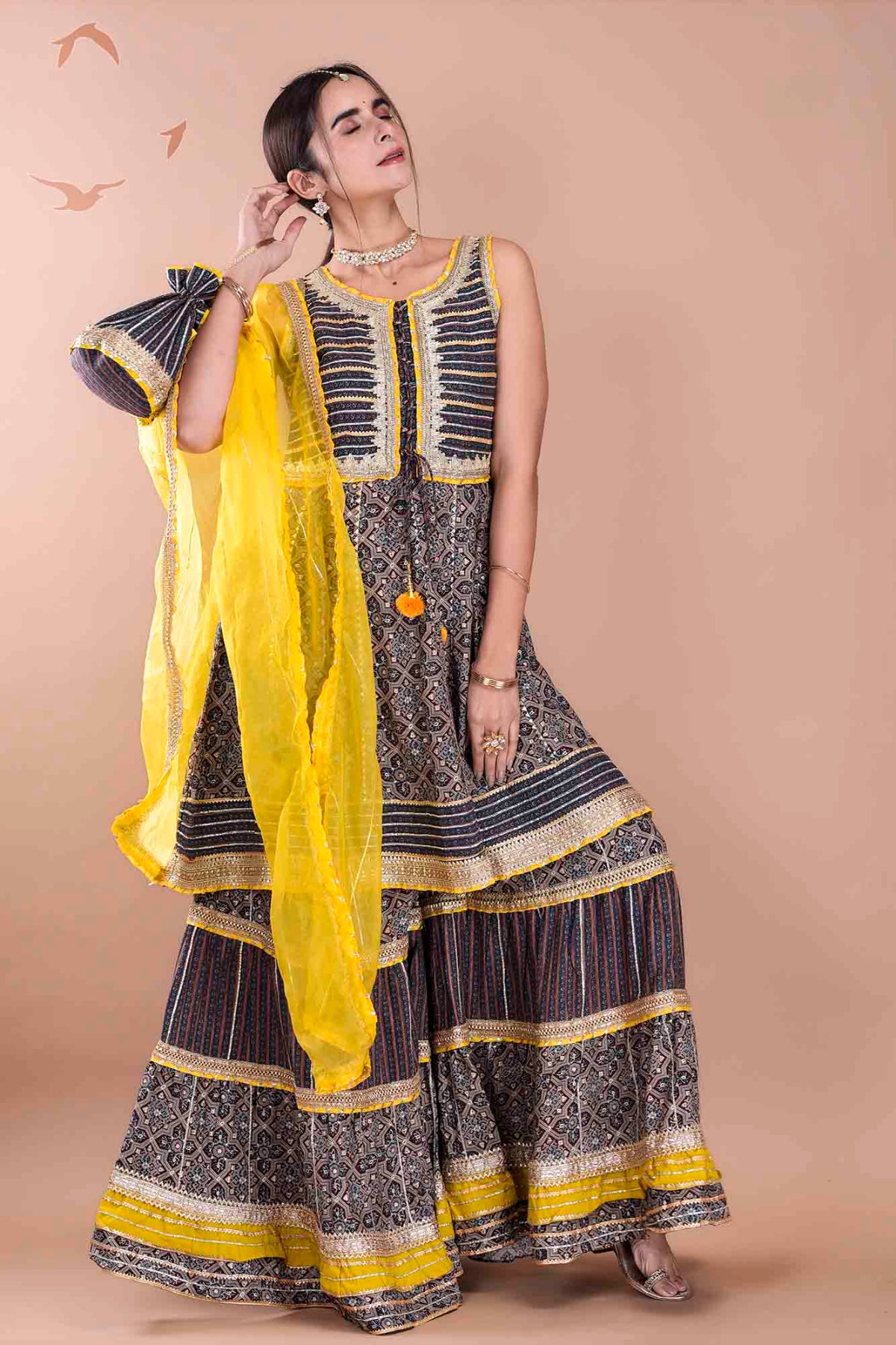 Woman wearing a traditional outfit with a yellow dupatta against a beige background