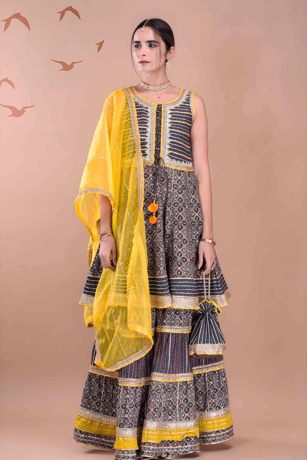 Woman wearing a traditional outfit with a yellow dupatta against a beige background