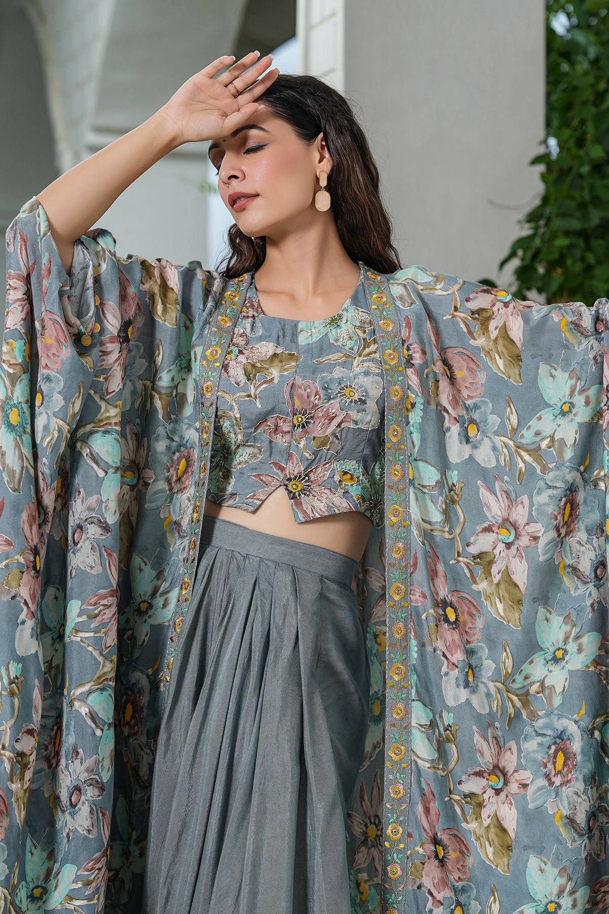 Woman wearing a floral blouse and gray pants with a floral shawl, standing outdoors.