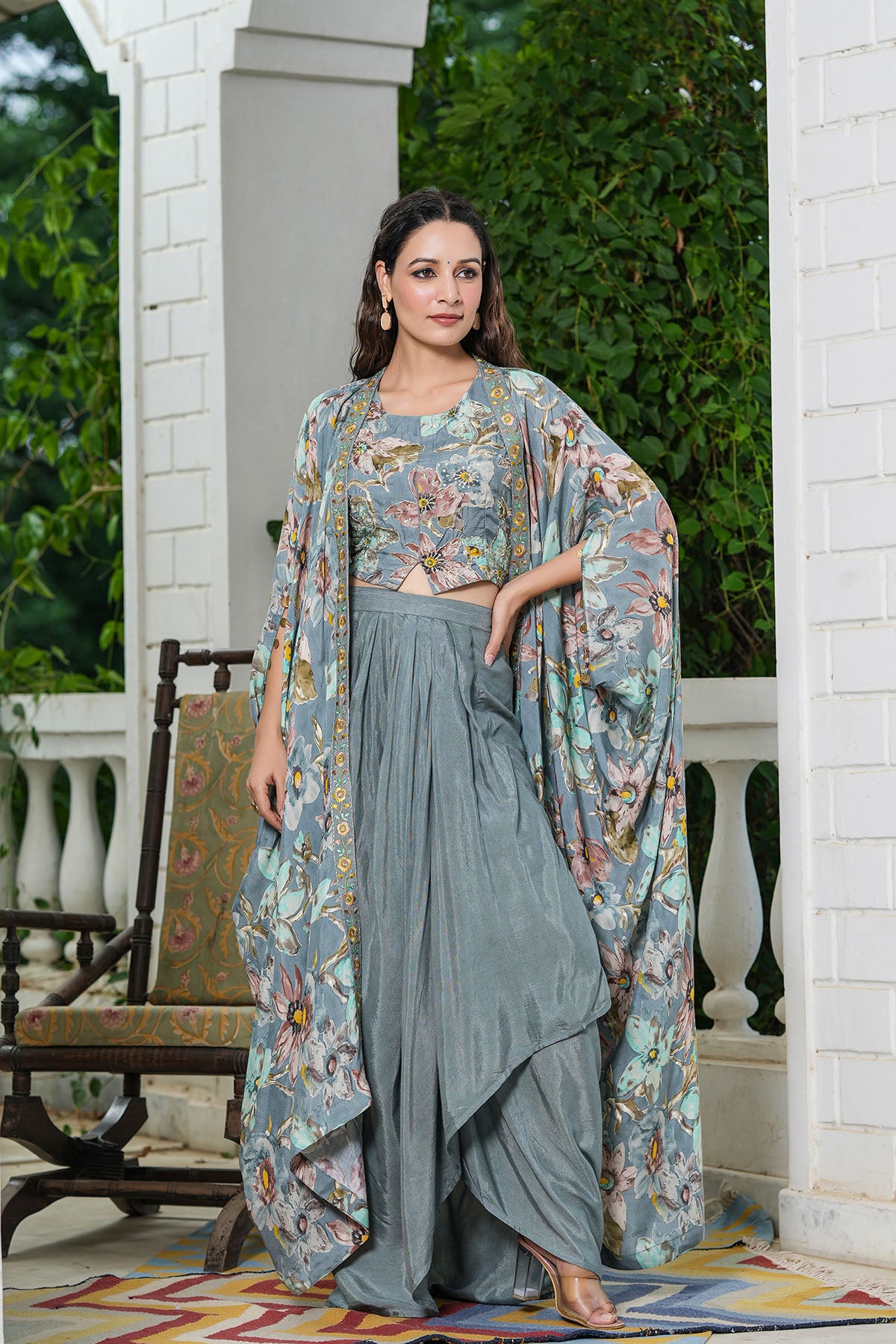 Woman in a floral outfit standing on a porch with greenery in the background