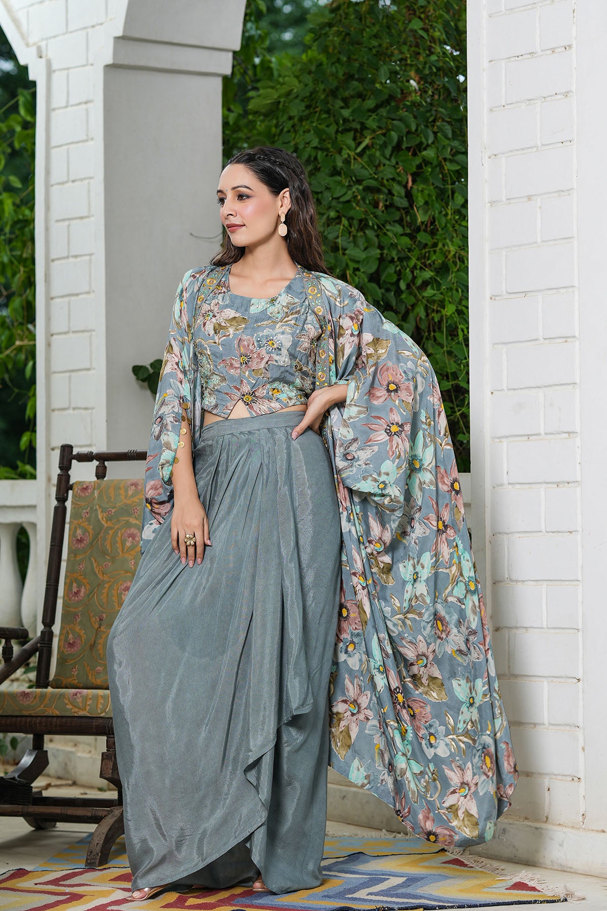 Woman in a floral outfit standing on a porch with greenery in the background