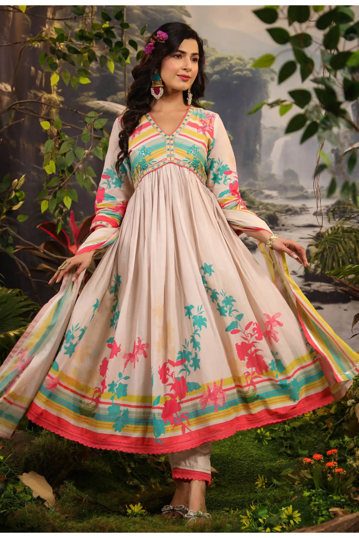 Woman in a colorful traditional outfit standing in a natural setting with trees and plants.