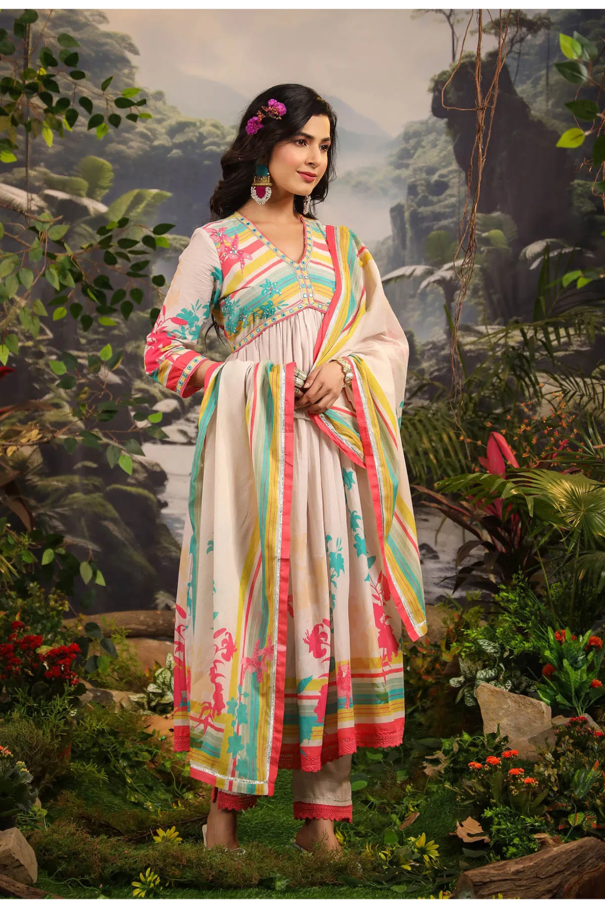 Woman in a colorful traditional outfit standing in a lush, green outdoor setting.