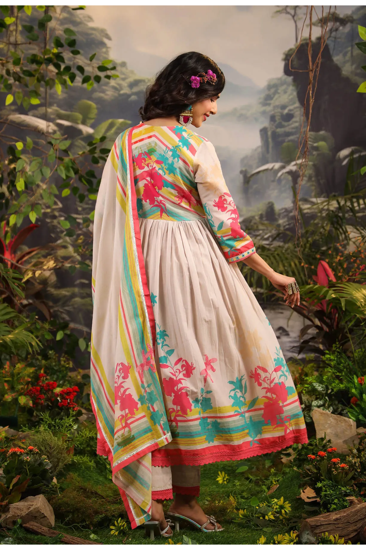 Woman in a colorful dress standing in a natural setting with mountains and plants.