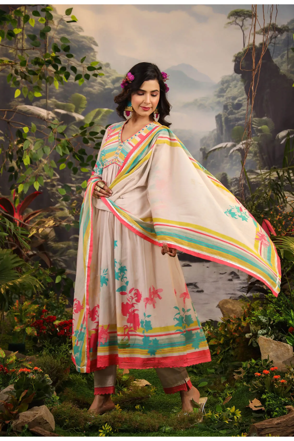 Woman in a colorful traditional outfit standing in a natural setting with mountains and water.