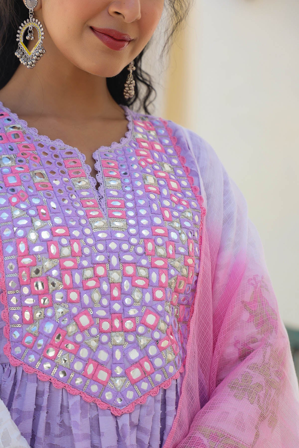 Close-up of a person wearing a purple and pink embroidered top with a blurred background