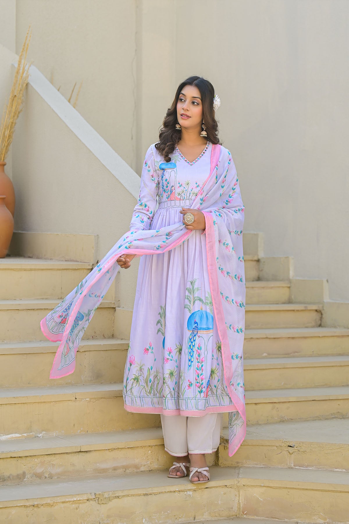 Woman in a light purple traditional outfit with floral patterns standing on steps.