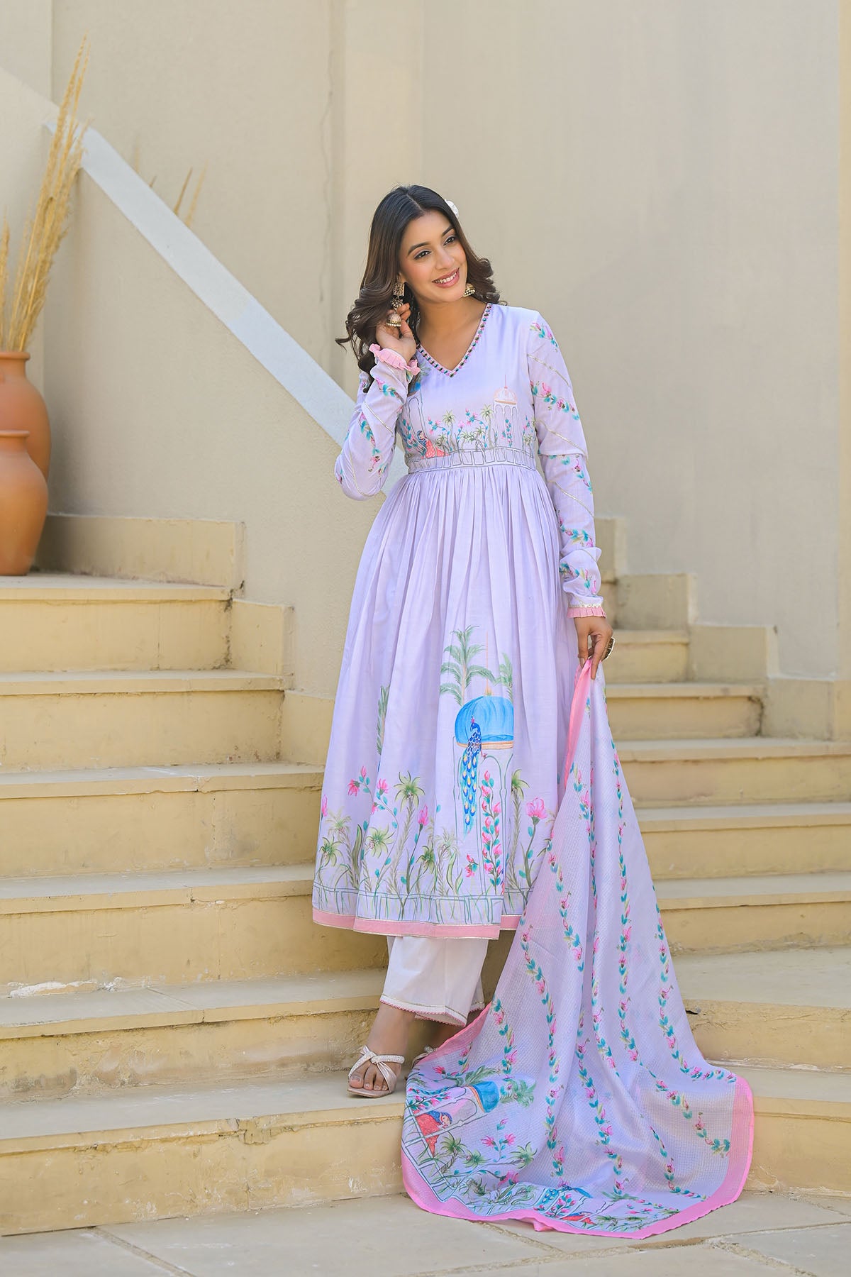 Woman in a light purple traditional outfit with floral patterns standing on steps.