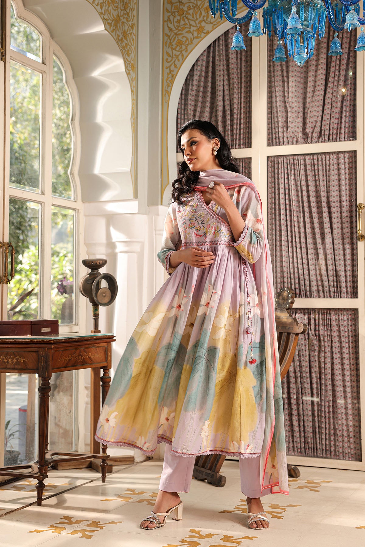 Woman in a colorful traditional outfit standing in a room with large windows and decorative elements.