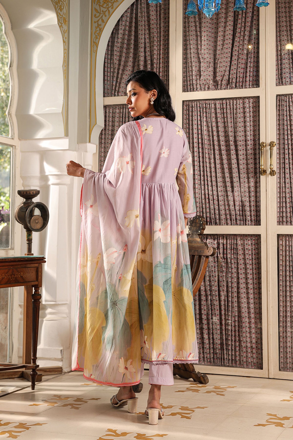 Woman in a colorful dress standing in a decorated room with patterned curtains and furniture.