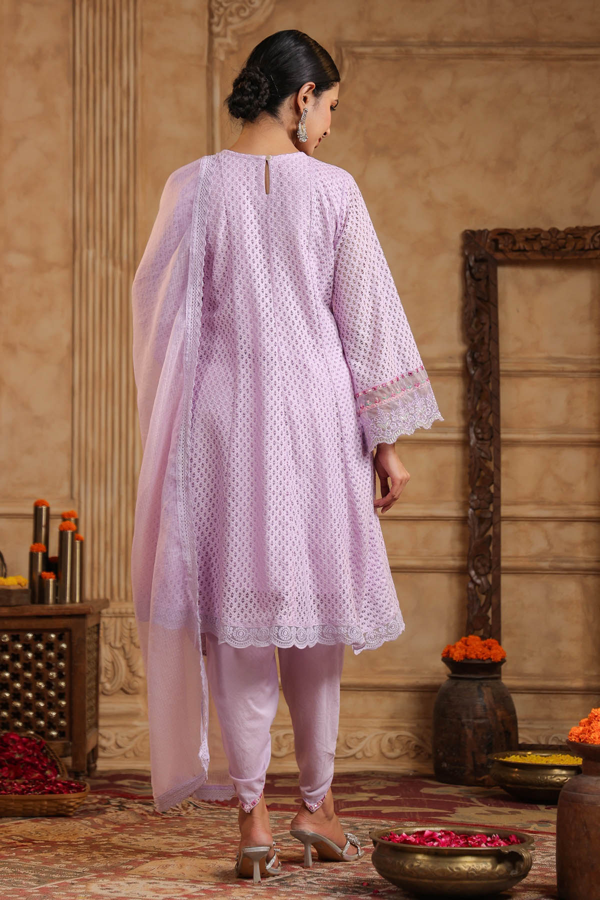 Woman in a light pink traditional outfit standing in a decorated room with floral arrangements.