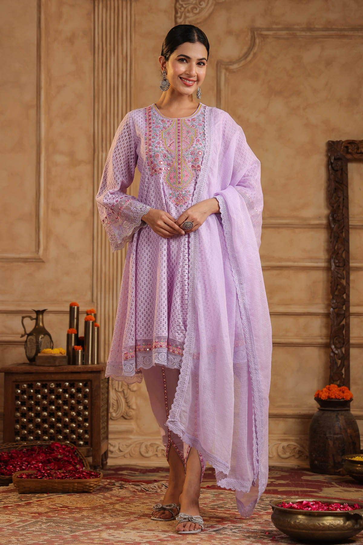 Woman in a light purple traditional outfit standing in an ornate room.