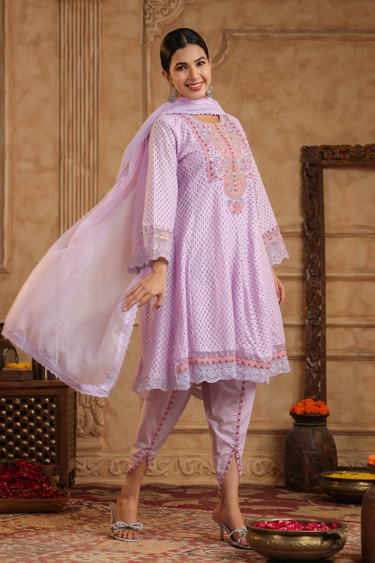 Woman in a light pink traditional outfit with embroidery in an ornate room.