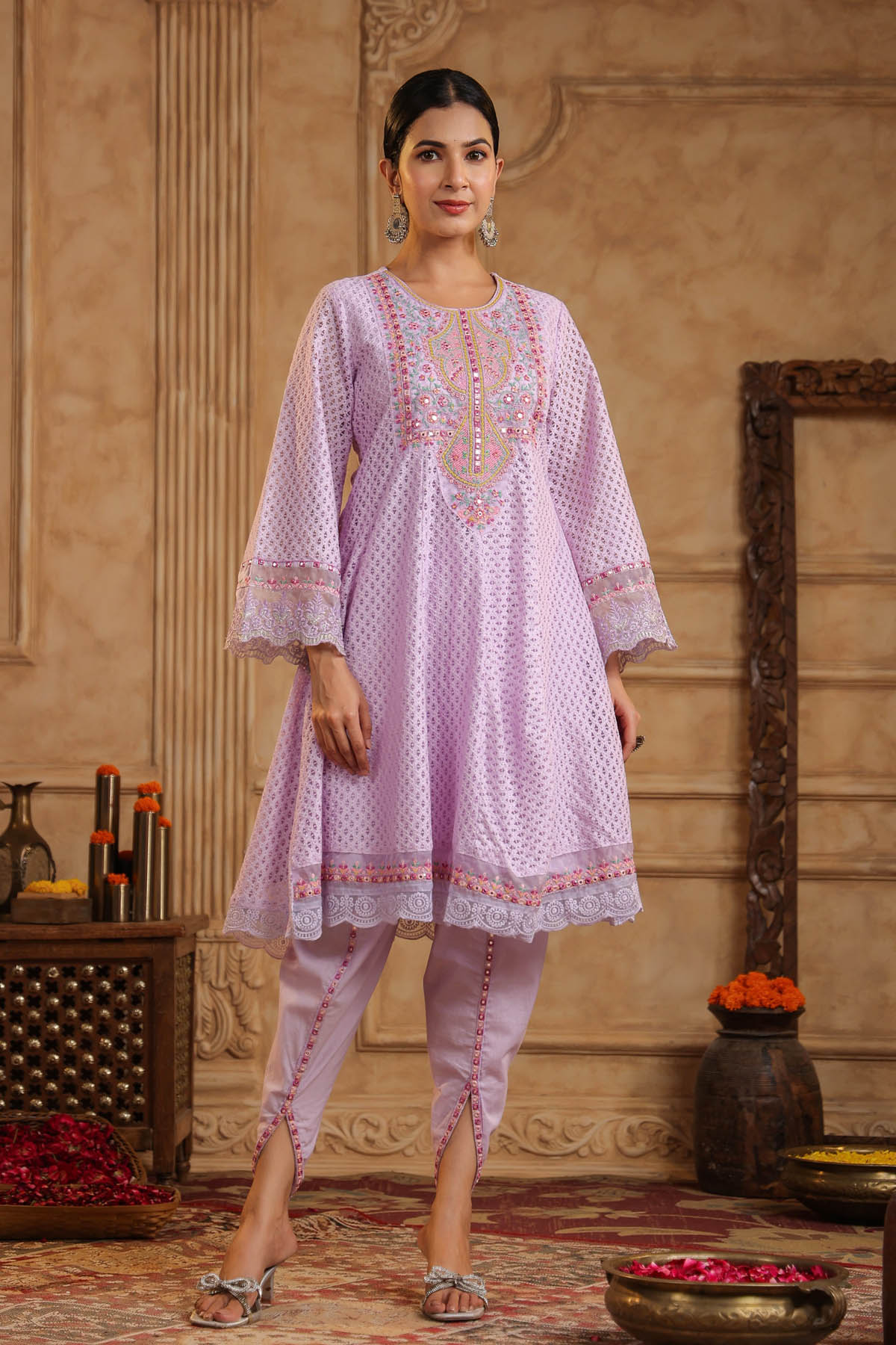 Woman wearing a light purple embroidered traditional outfit in an ornate room.