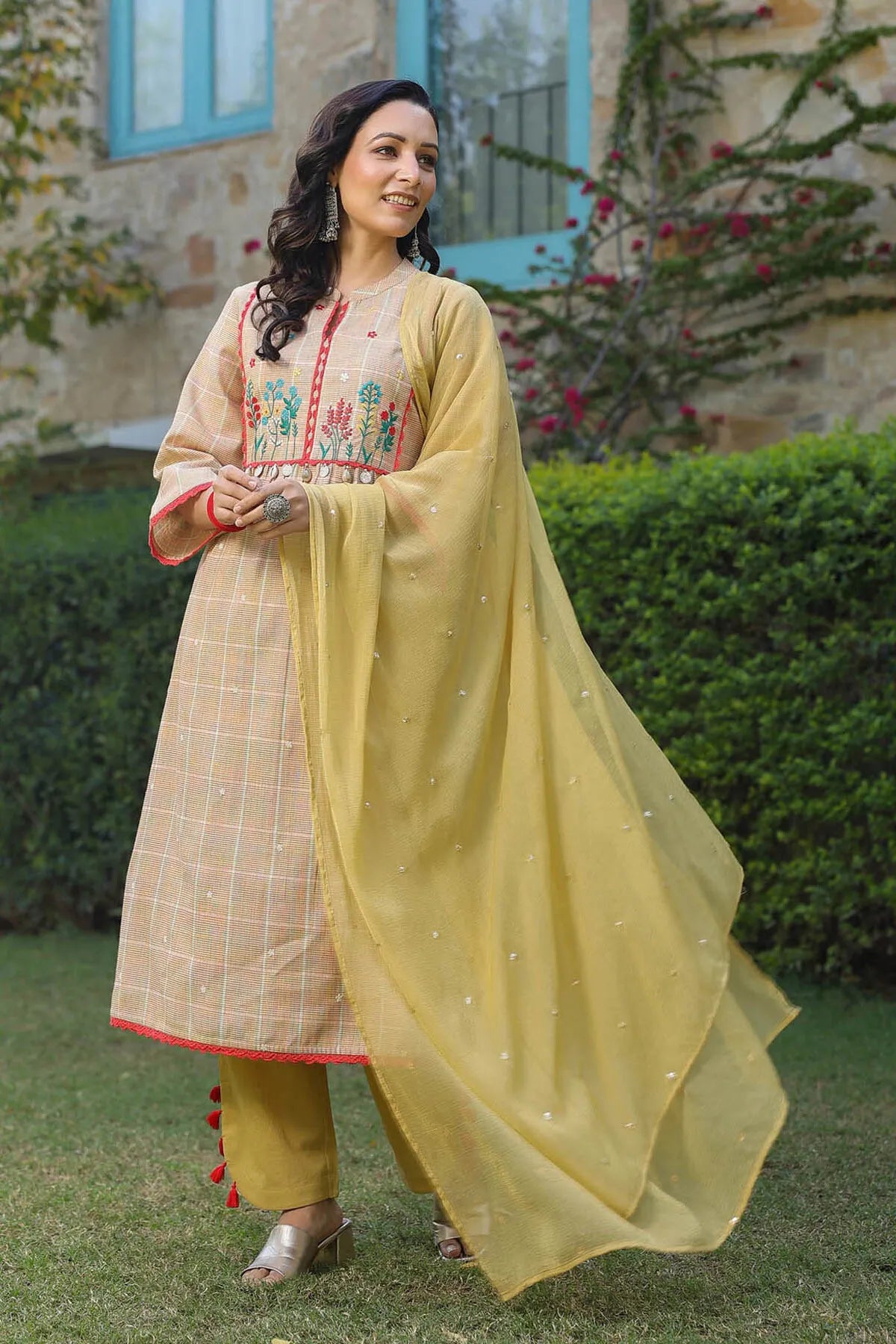 Woman in traditional outfit with embroidered top and yellow dupatta standing outdoors.