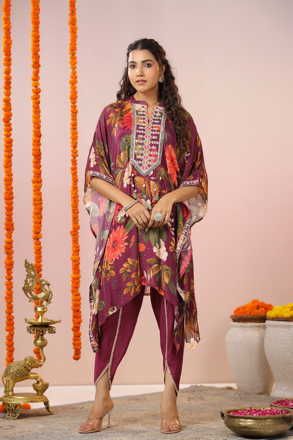 Woman wearing a colorful traditional outfit with floral patterns against a pink background.
