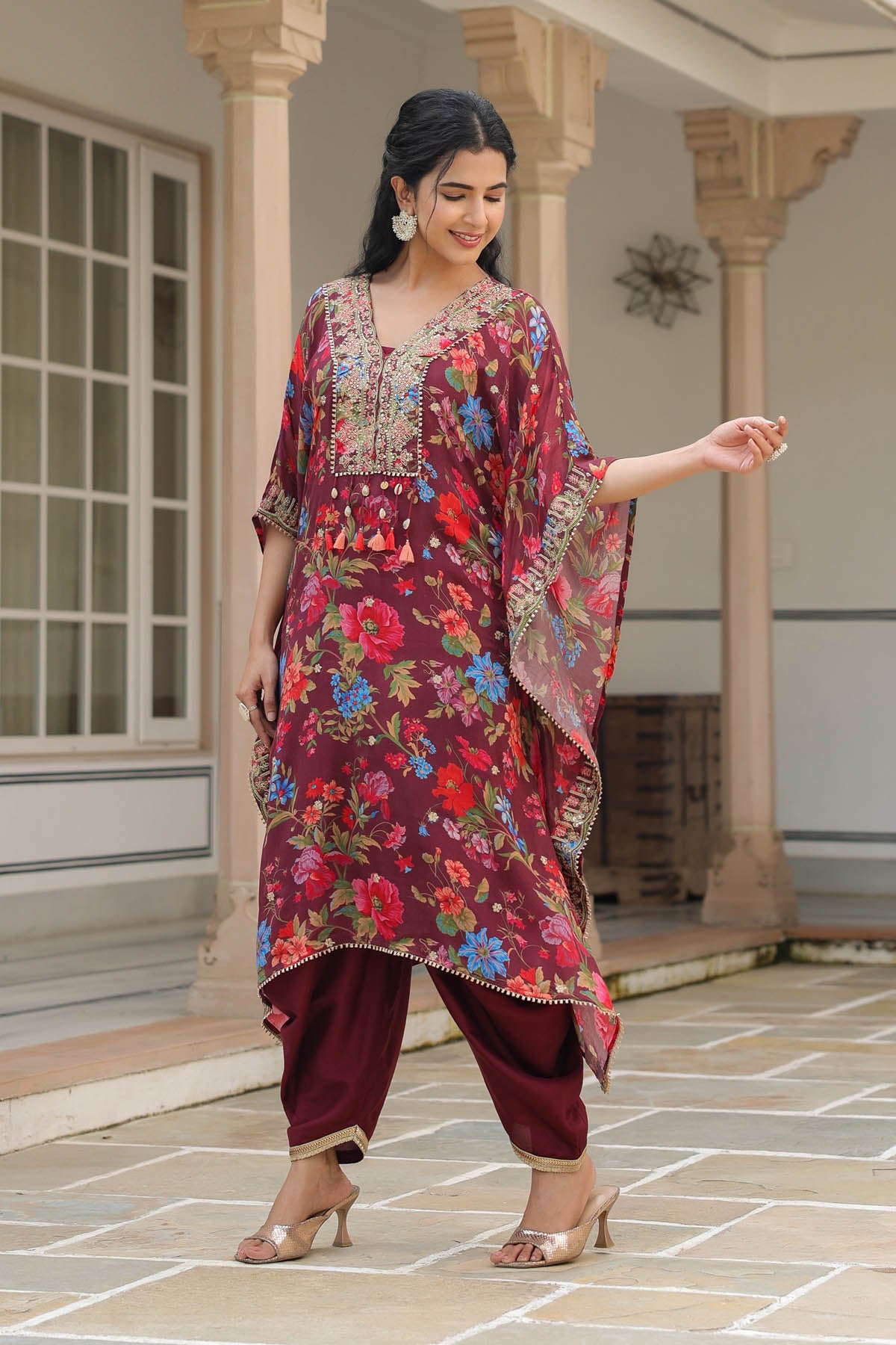 Woman wearing a colorful floral dress with a traditional design, standing on a stone pavement.