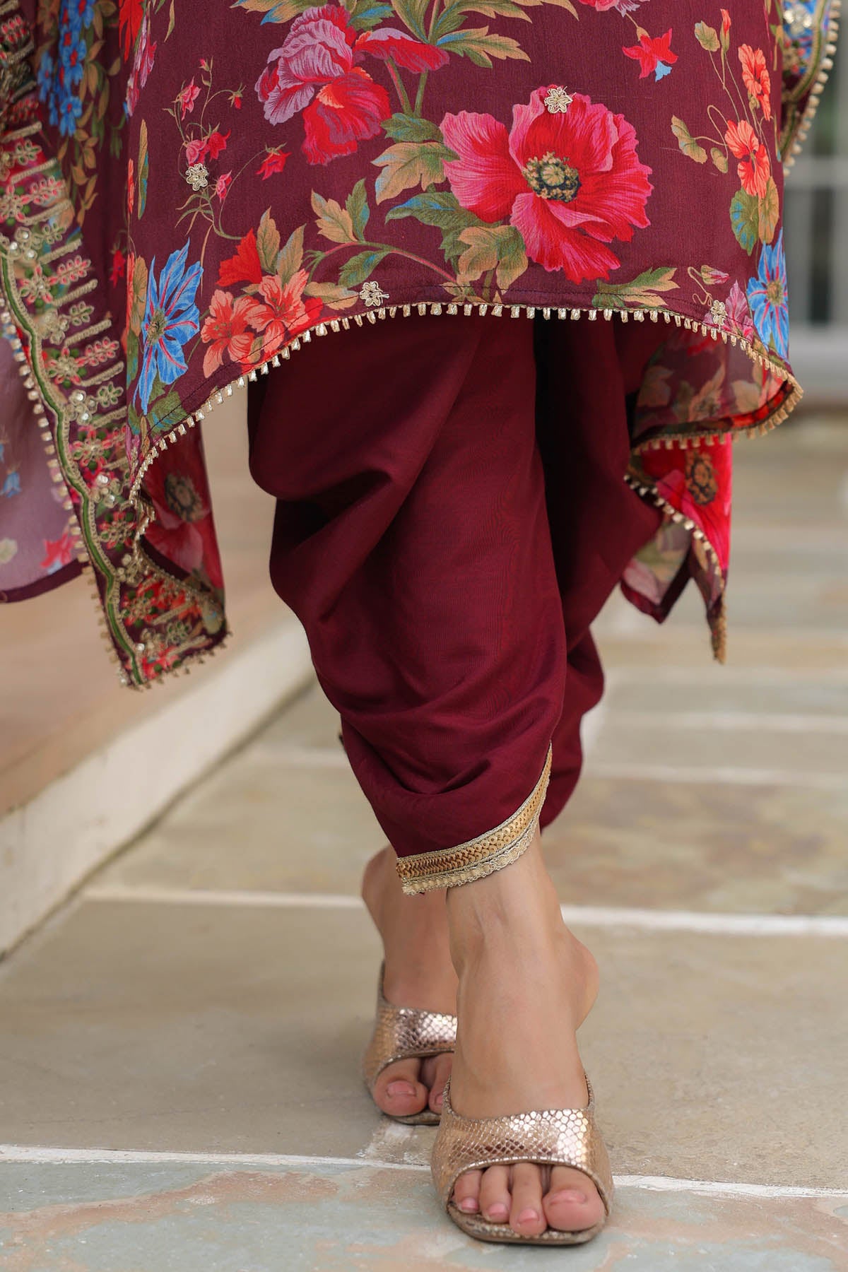 Maroon traditional outfit with floral embroidery and gold sandals on a neutral background