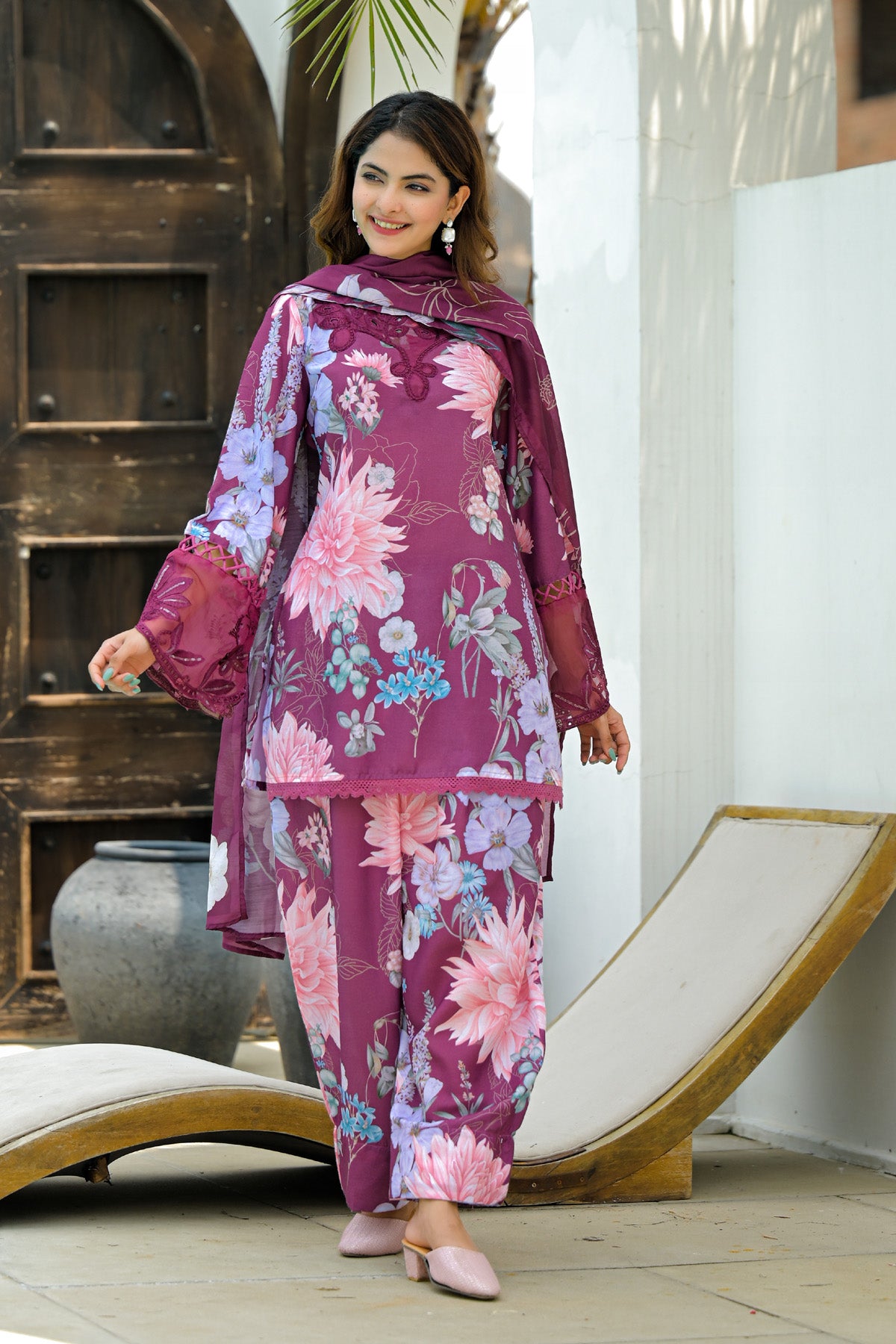 Woman wearing a floral pink and purple traditional outfit standing in a sunlit outdoor setting.