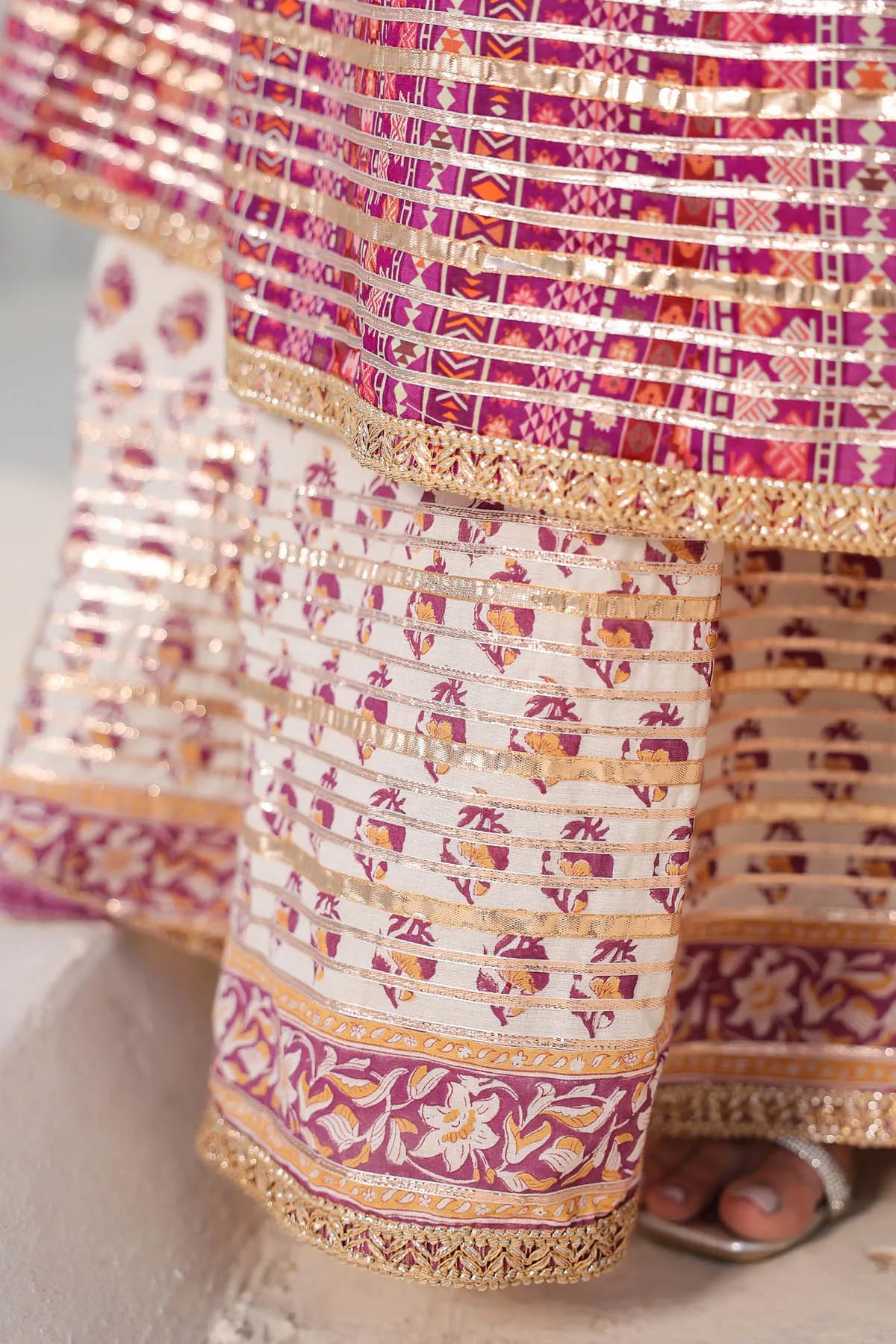 Close-up of a traditional patterned fabric with pink, purple, and gold colors.