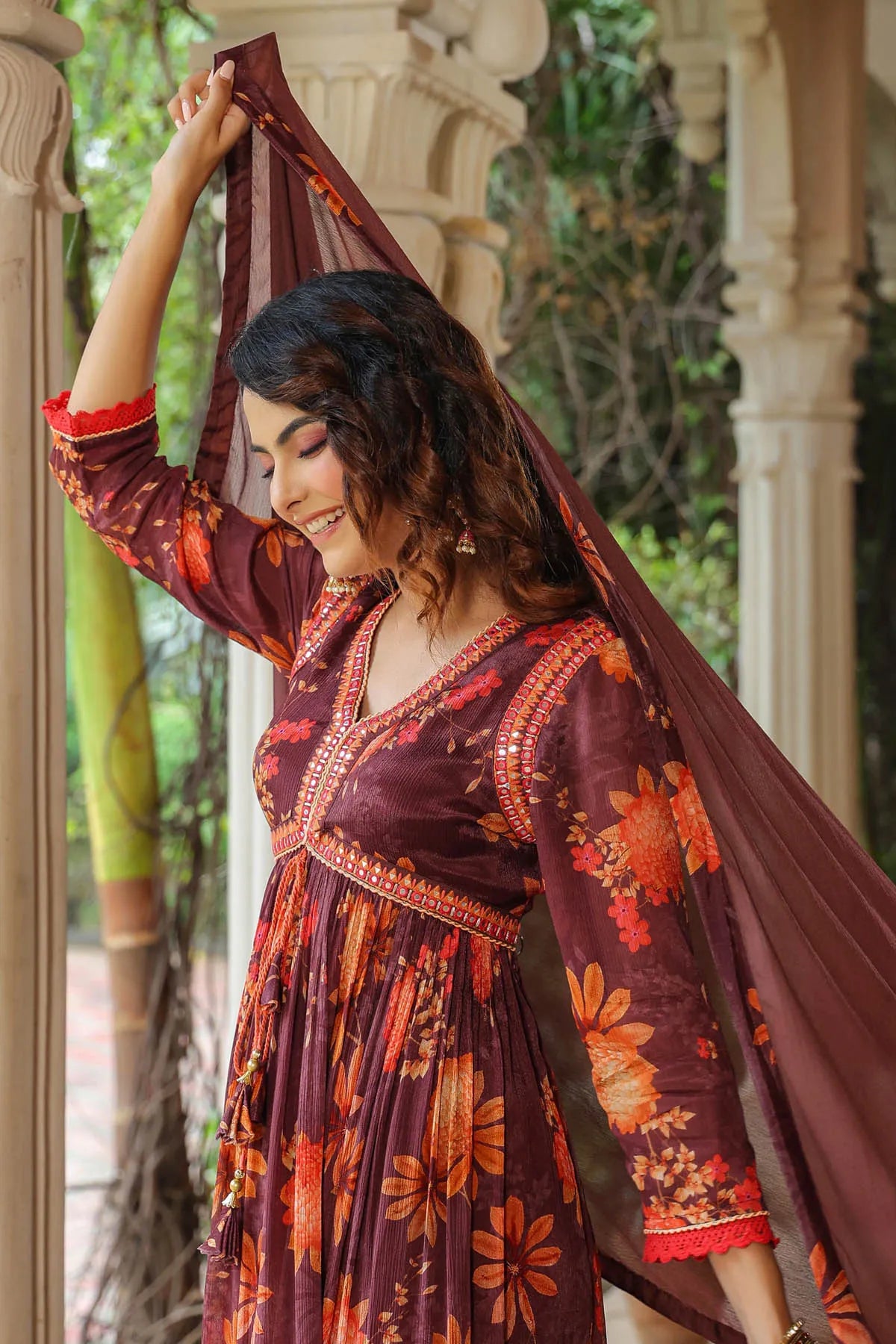 Woman in a floral dress with a long scarf, standing in an outdoor setting.