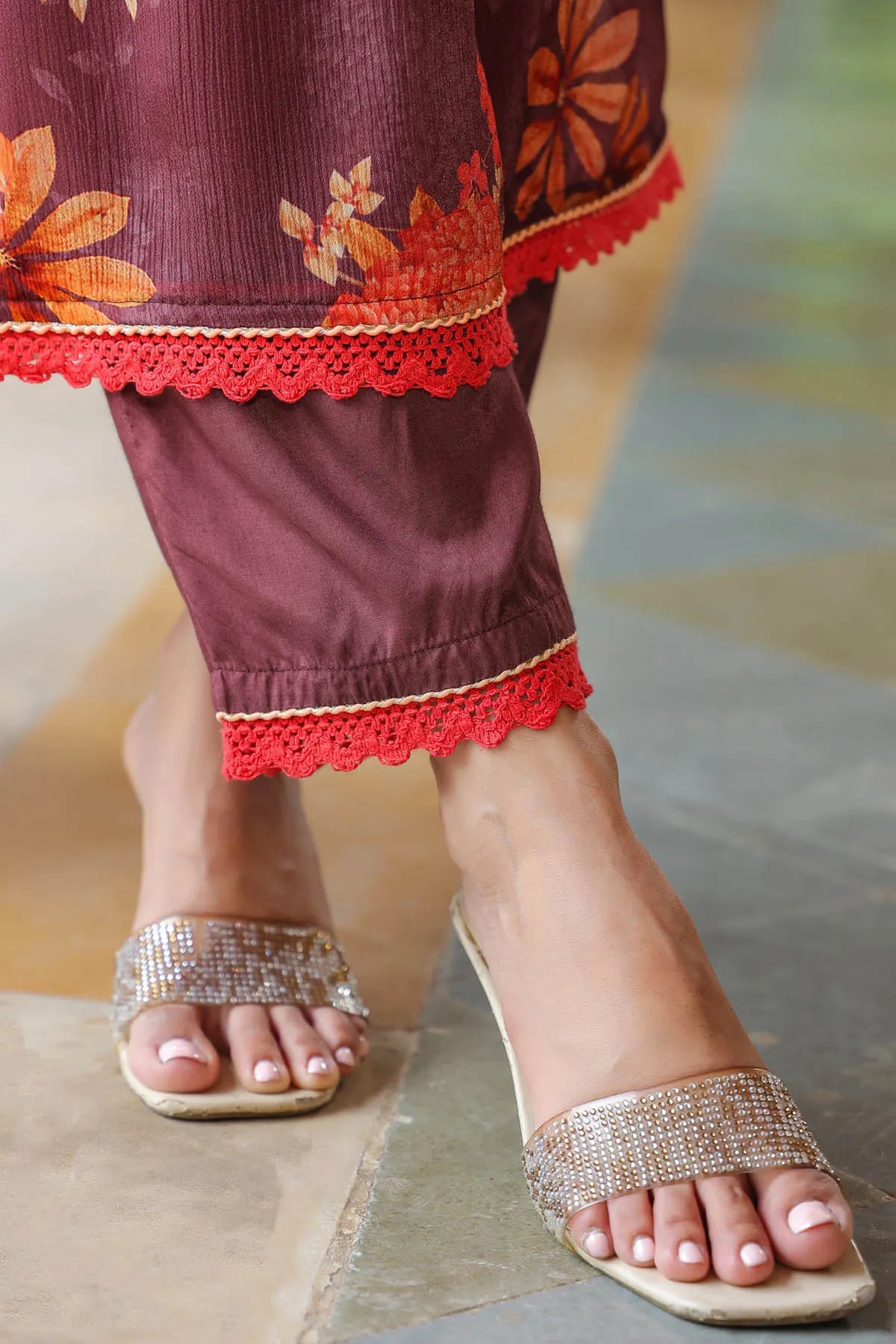 Close-up of feet wearing sandals with decorative straps, standing on a textured surface.
