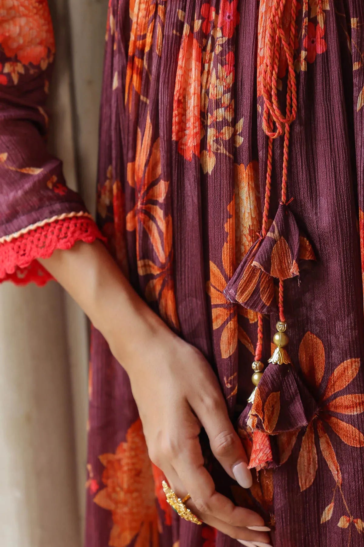 Close-up of a hand holding a purple garment with floral patterns and tassels.