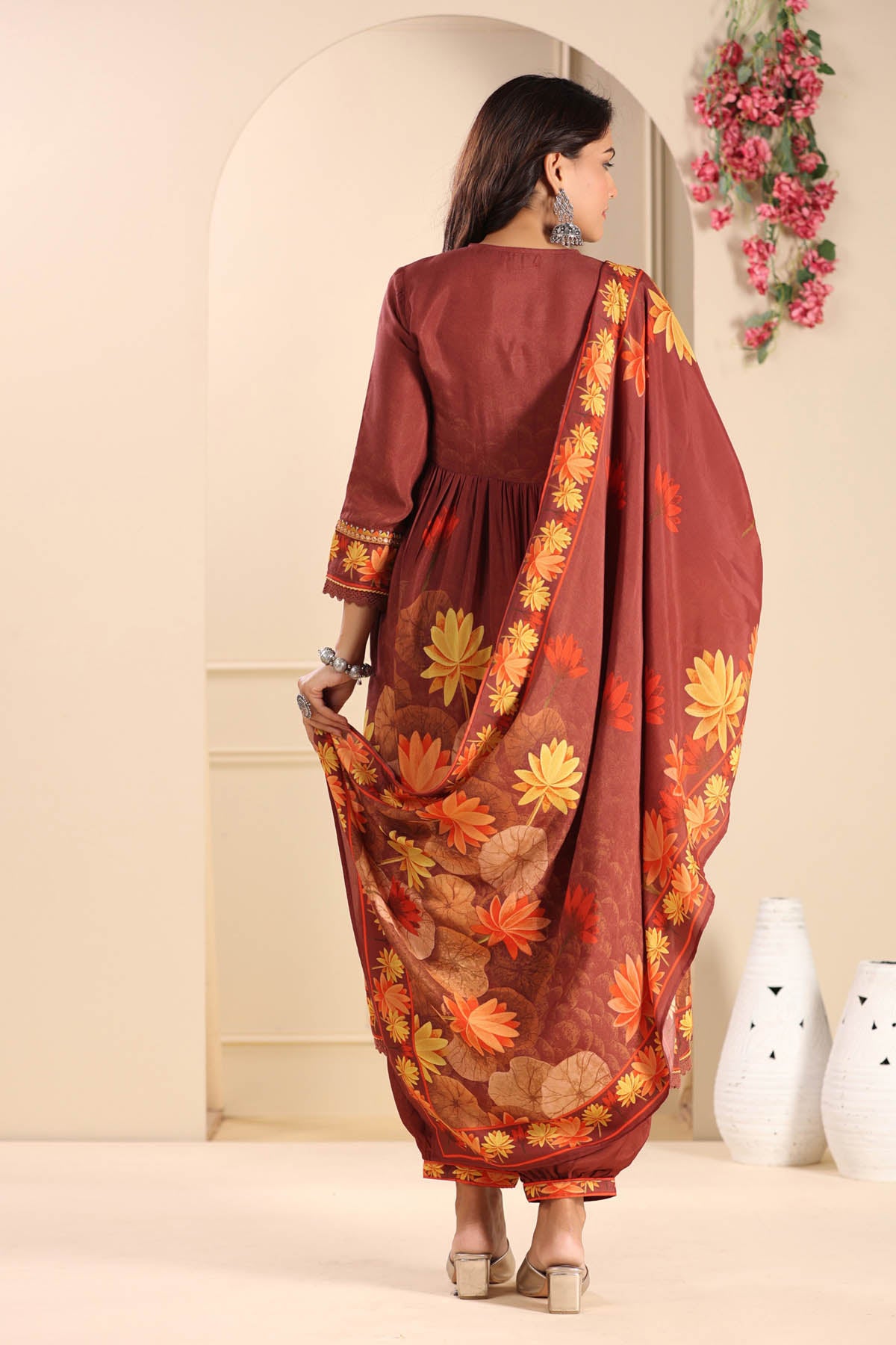 Woman wearing a brown traditional outfit with floral patterns in a room.
